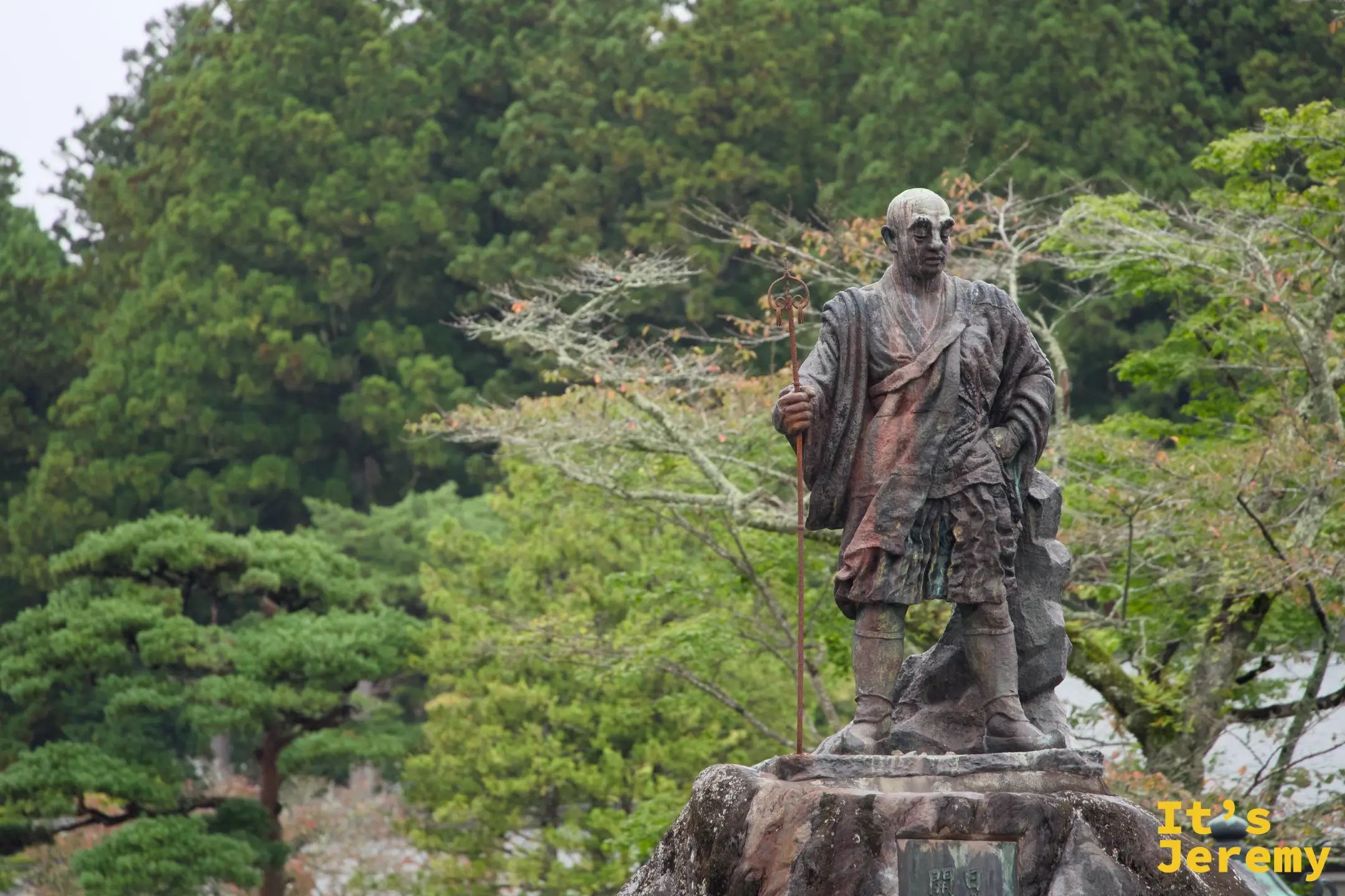 輪王寺境內的勝道上人銅像，手持錫杖，背後是日光山的杉木與楓樹