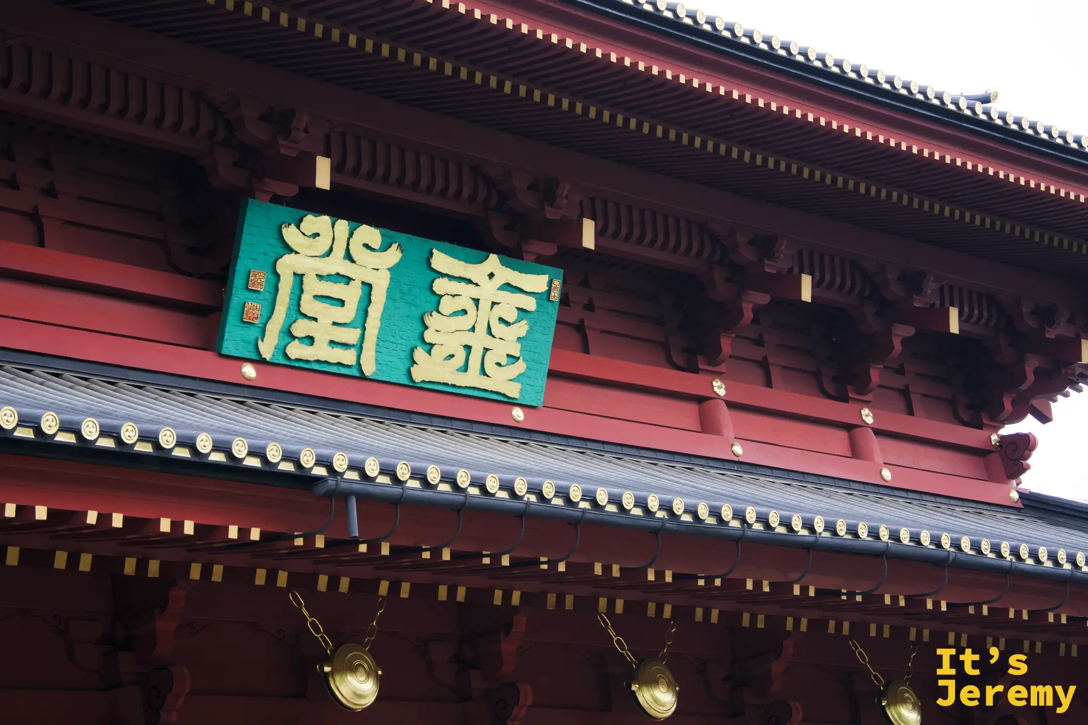 三仏堂正面，深紅外牆與綠底金字題匾，在表參道末端顯得體積龐大