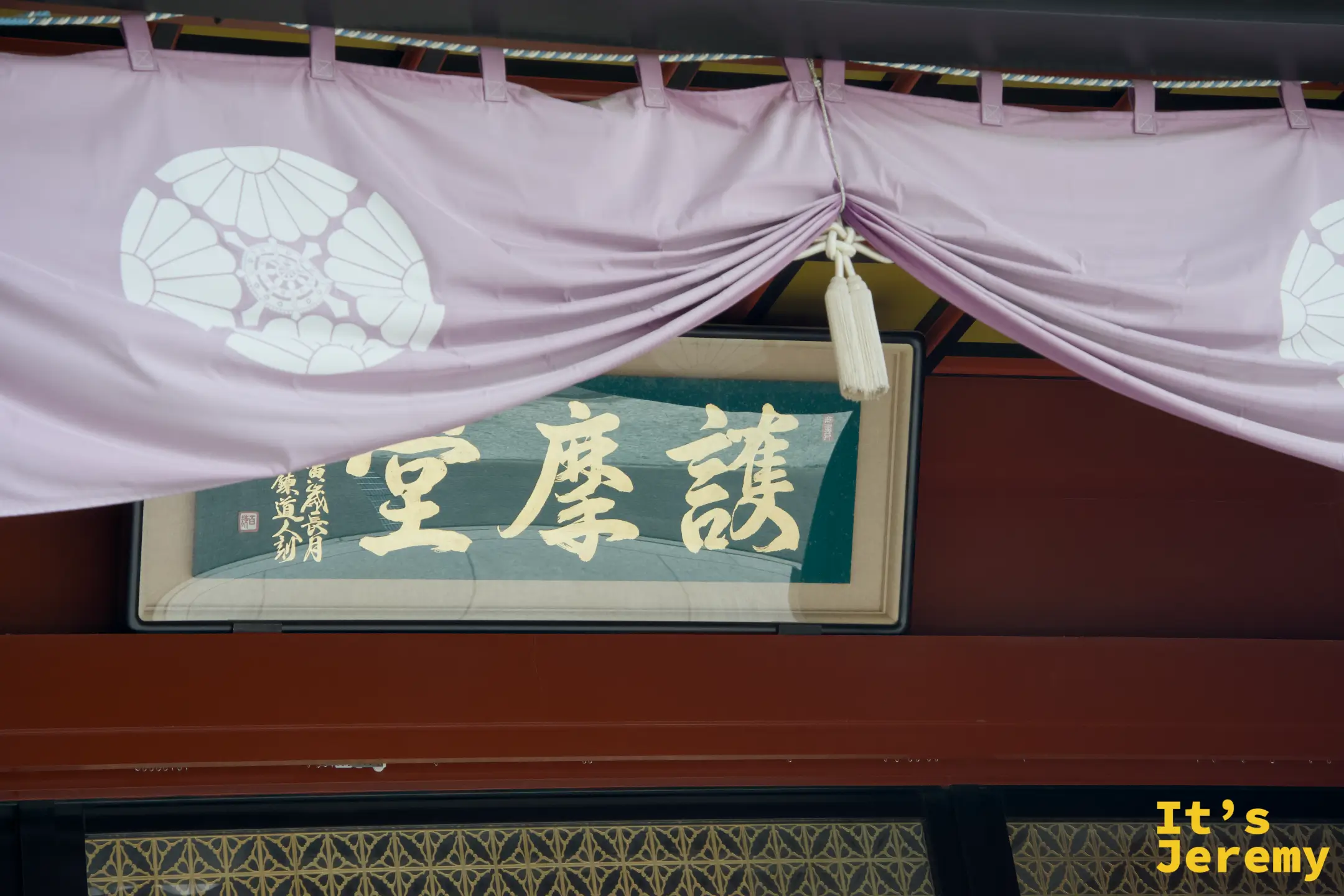 護摩堂入口「護摩堂」題匾，上方垂著印有家紋的白地紫幔，門板透著格紋花樣