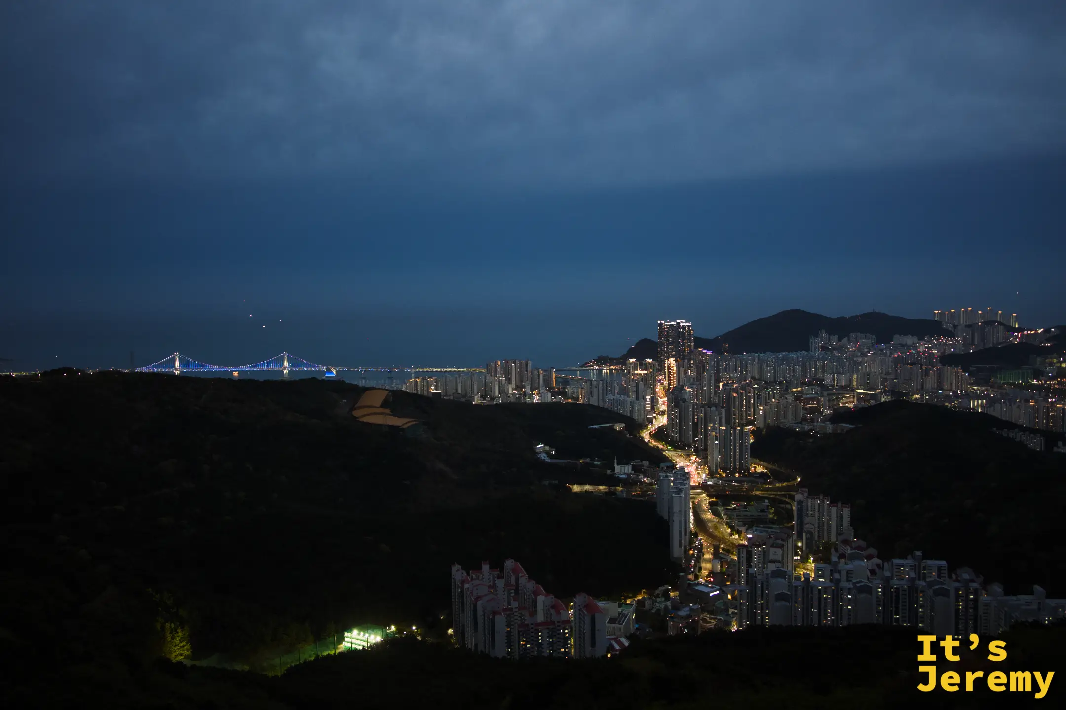 藍調時刻，廣安大橋的懸索弧線在深藍天空下清晰浮現，城市燈帶三層次鋪陳
