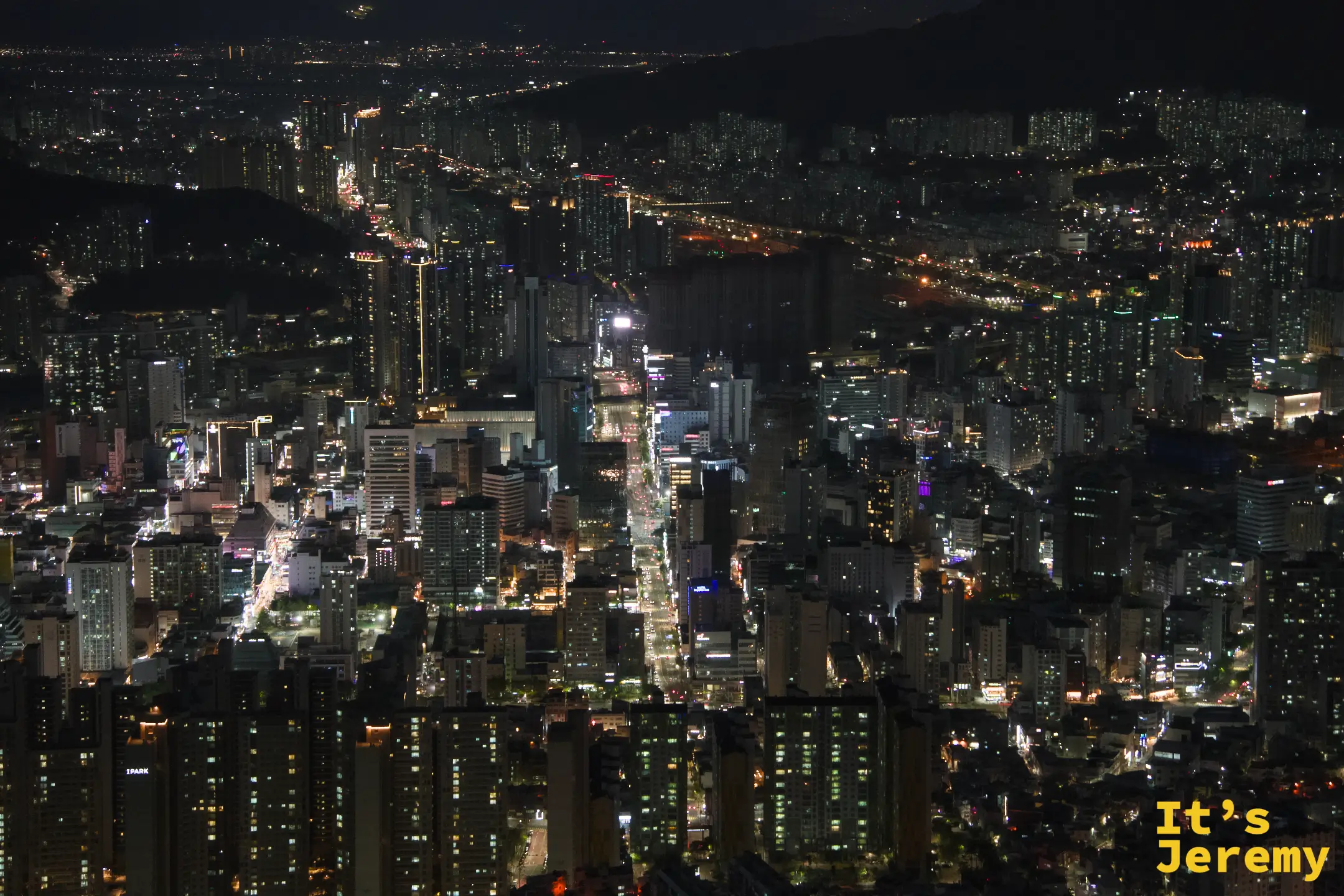 拉長焦距俯瞰釜山市區，道路燈帶被壓縮成幾條平行光線，城市密度一覽無遺