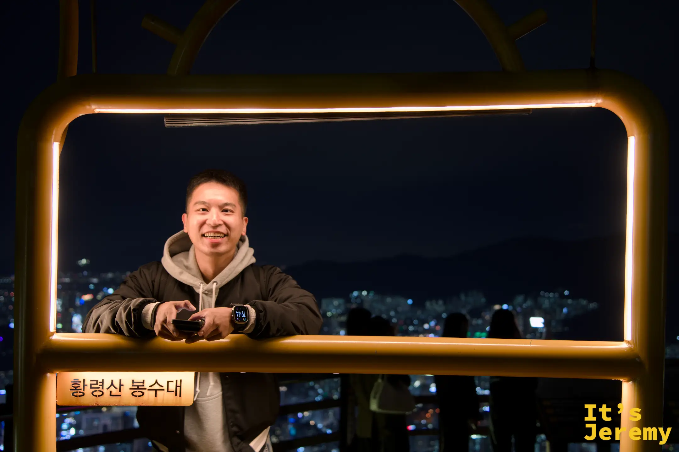 入夜後 LED 燈框自動亮起，暖黃色燈帶把框內的人打得恰到好處，背景的城市燈火遠到不搶鏡