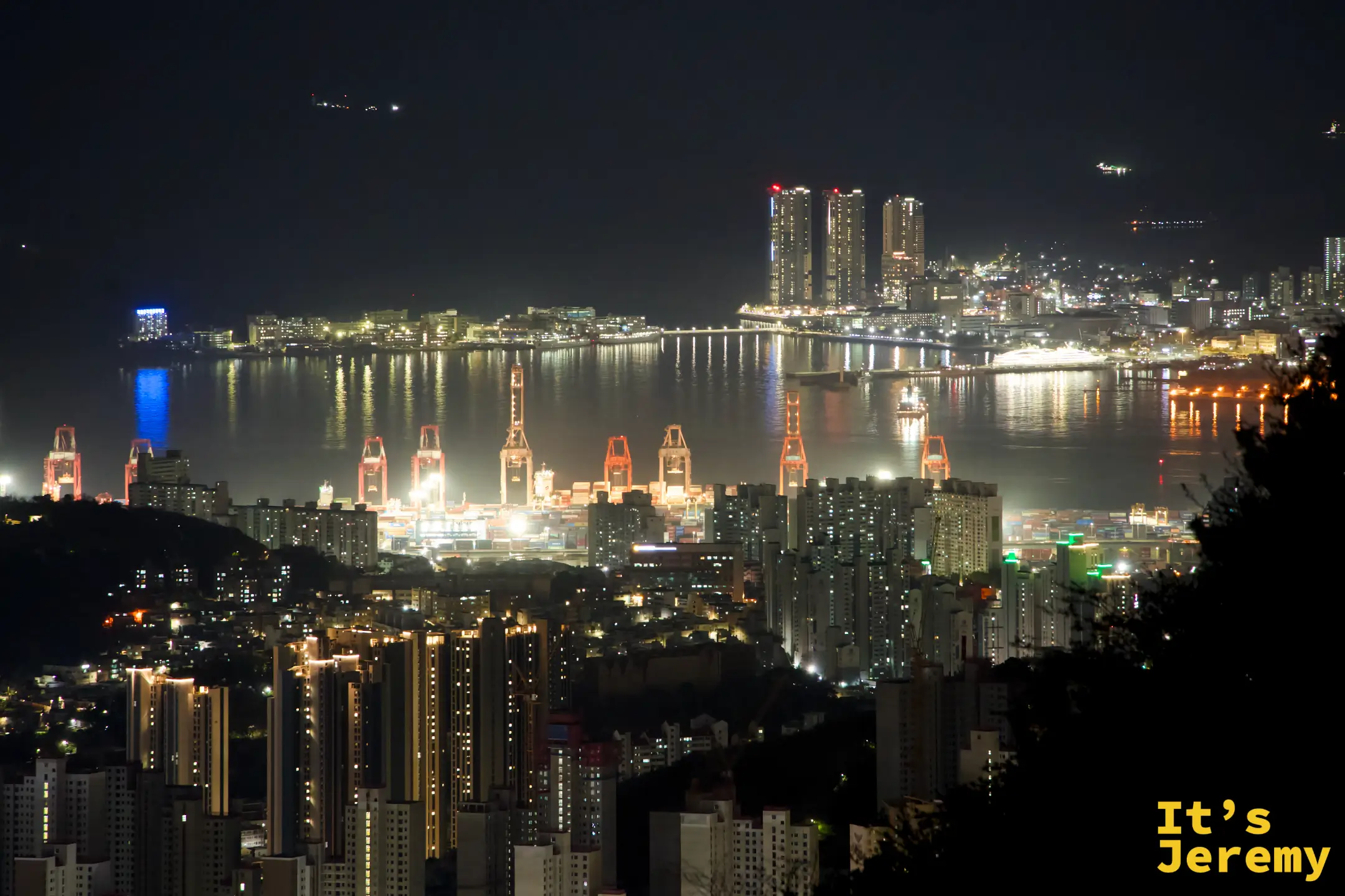 排列整齊的紅色起重機群倒影映在平靜港灣水面，工業場景多出一種意外的詩意