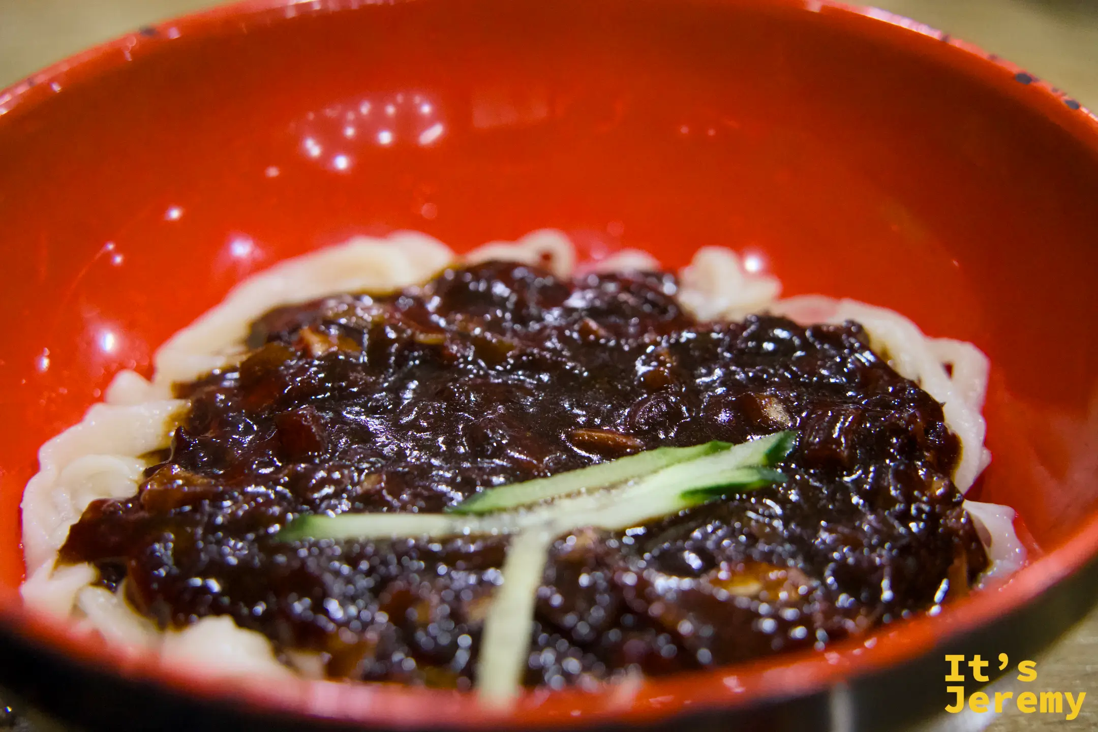 橘紅大碗裡的짜장면，漆黑豆醬厚覆在手切麵條上，點綴兩根黃瓜絲