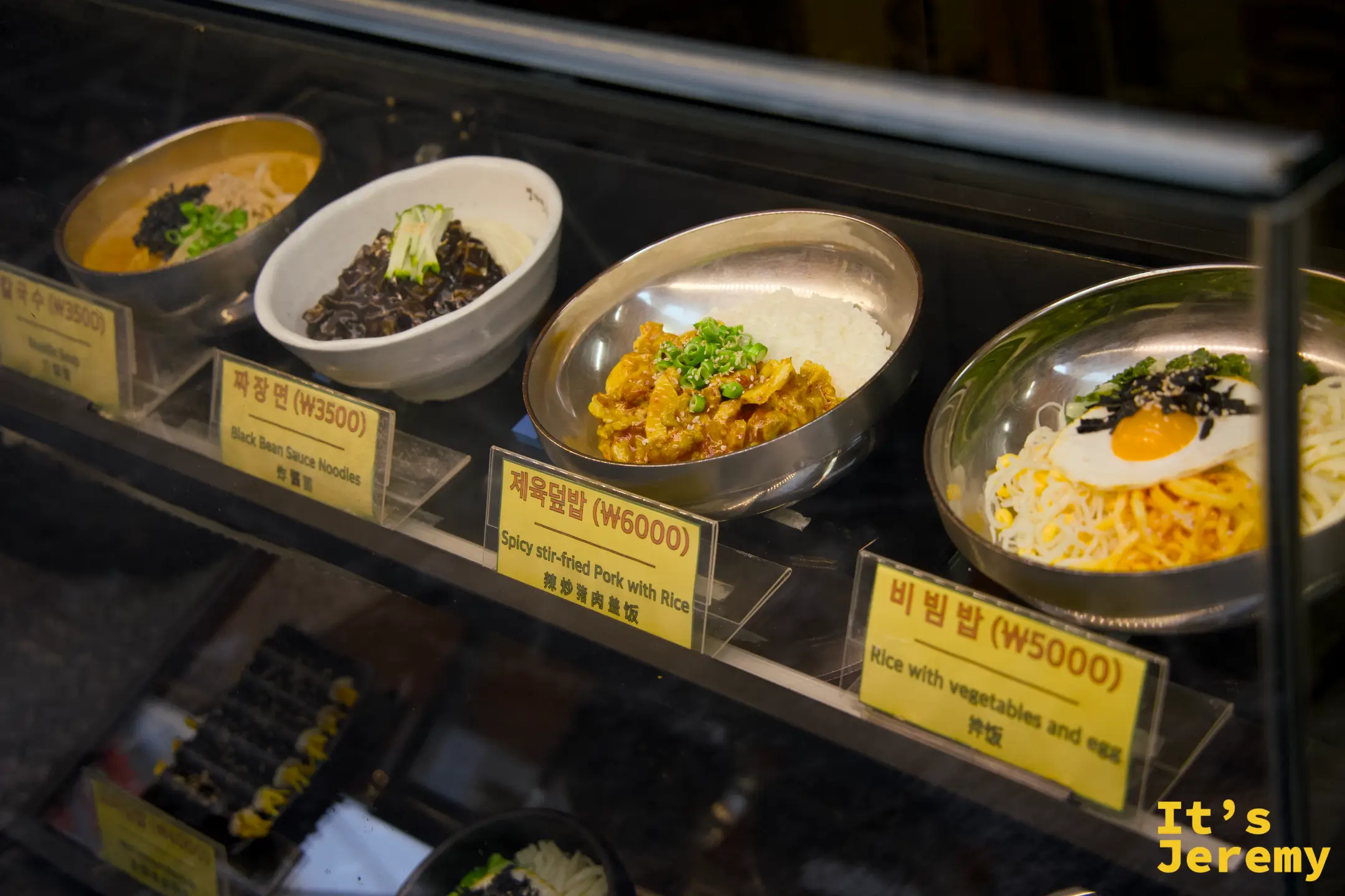 門口展示櫃的食物模型，清楚標示品項名稱與售價，中英日文對照