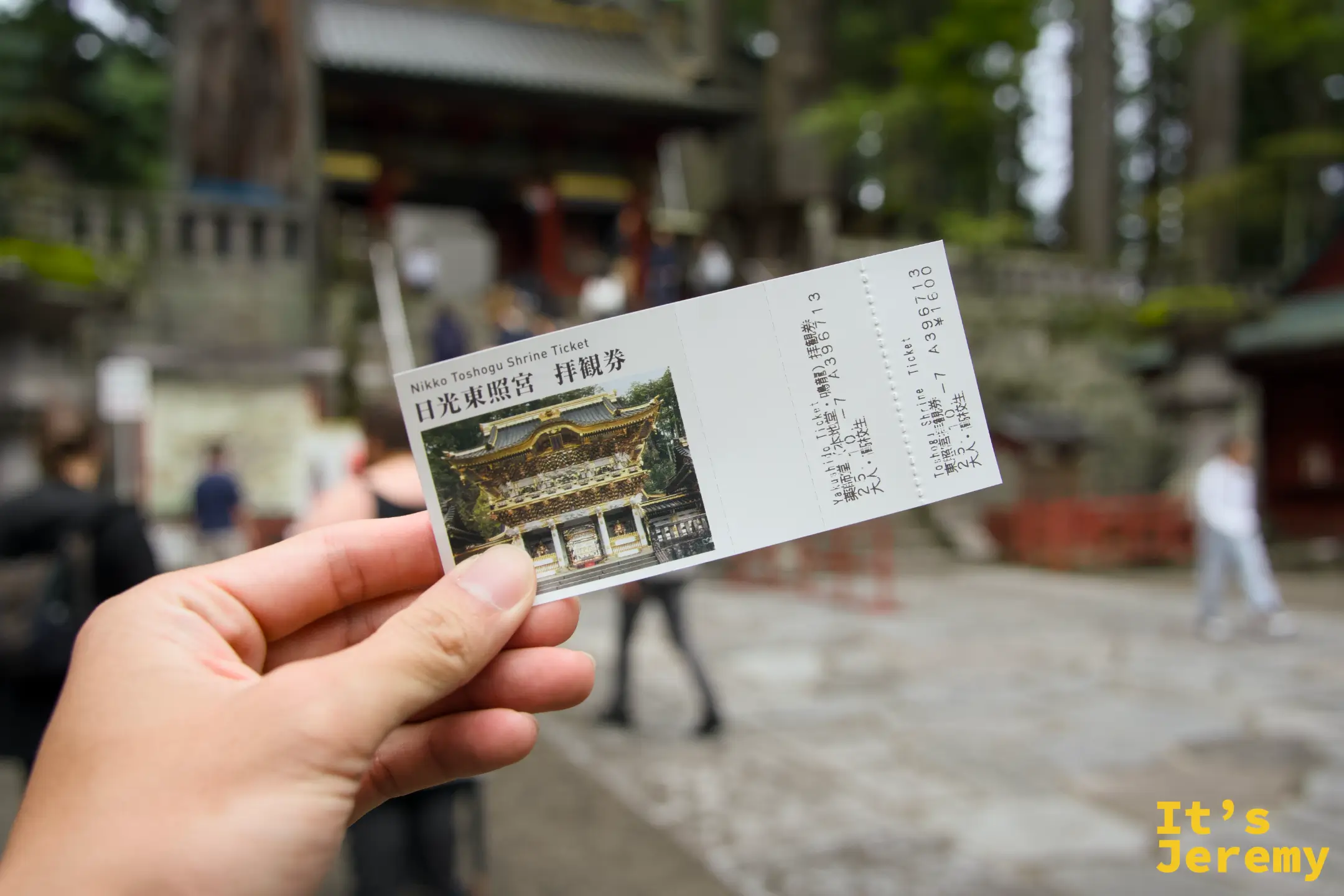 手持日光東照宮拜觀券，票面印有陽明門彩色圖案，背景是神社入口