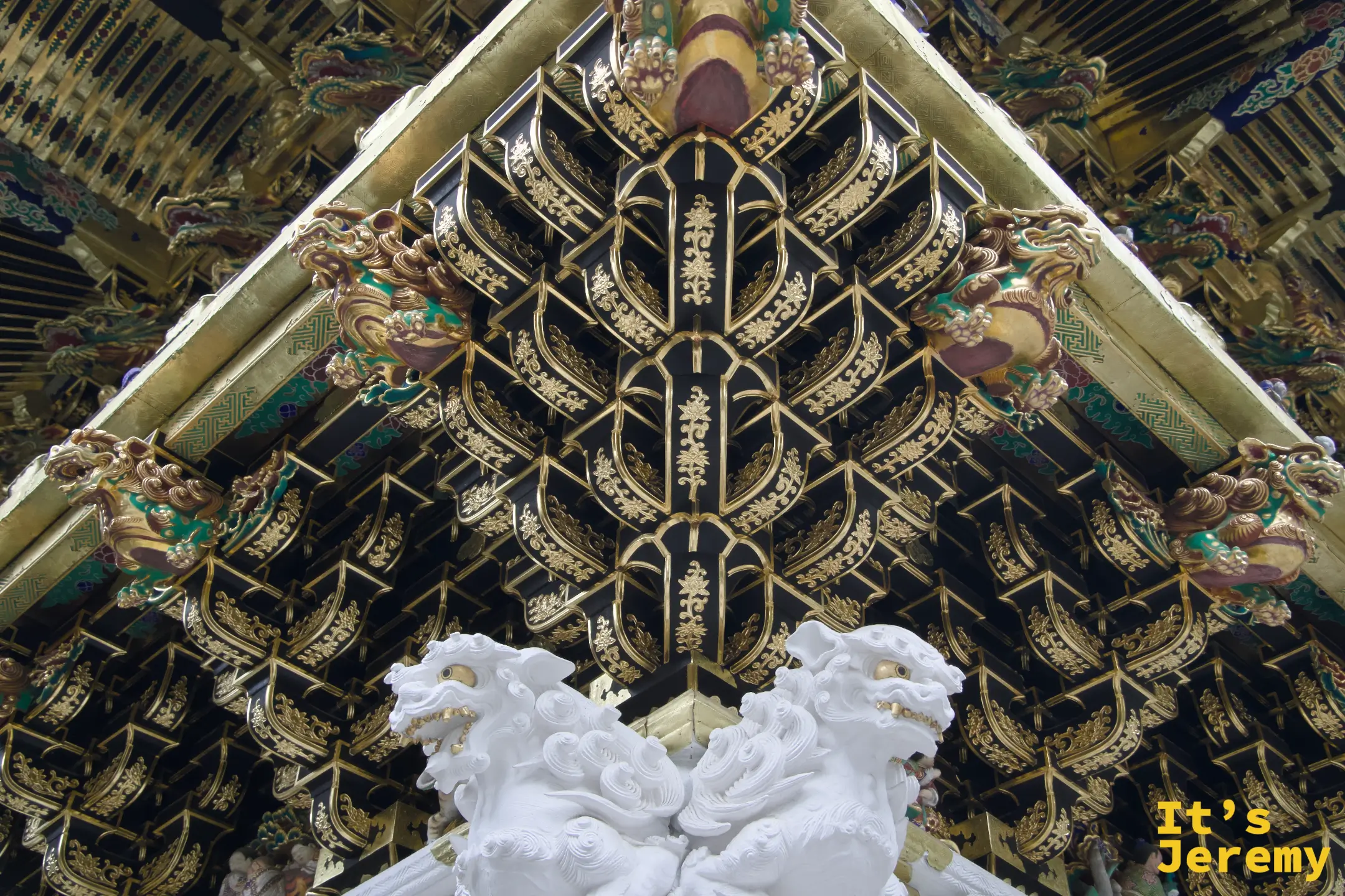 仰拍陽明門天花板藻井，金色幾何格紋從四角向中心收縮，下方立著一對白色狛犬