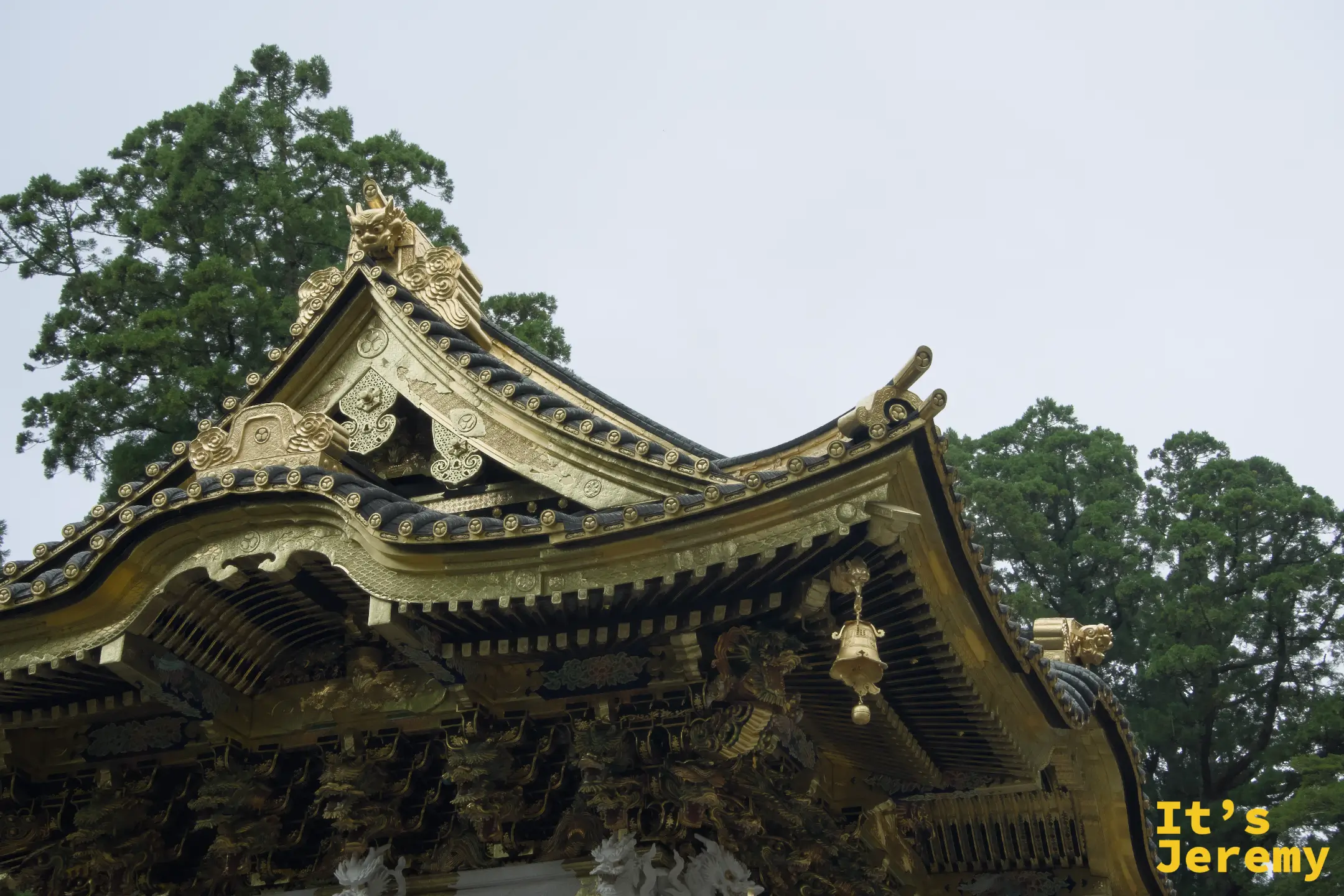 東照宮境內某棟建築的屋頂外觀，金黑配色的屋脊曲線舒展，屋簷下懸著銅鈴，兩側杉木為背景