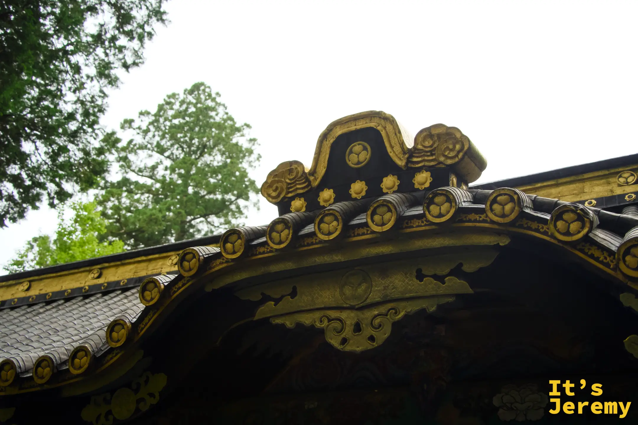 屋頂屋脊瓦片近景，每片瓦端均壓著三葉葵家紋，排列整齊，底色為黑金兩色