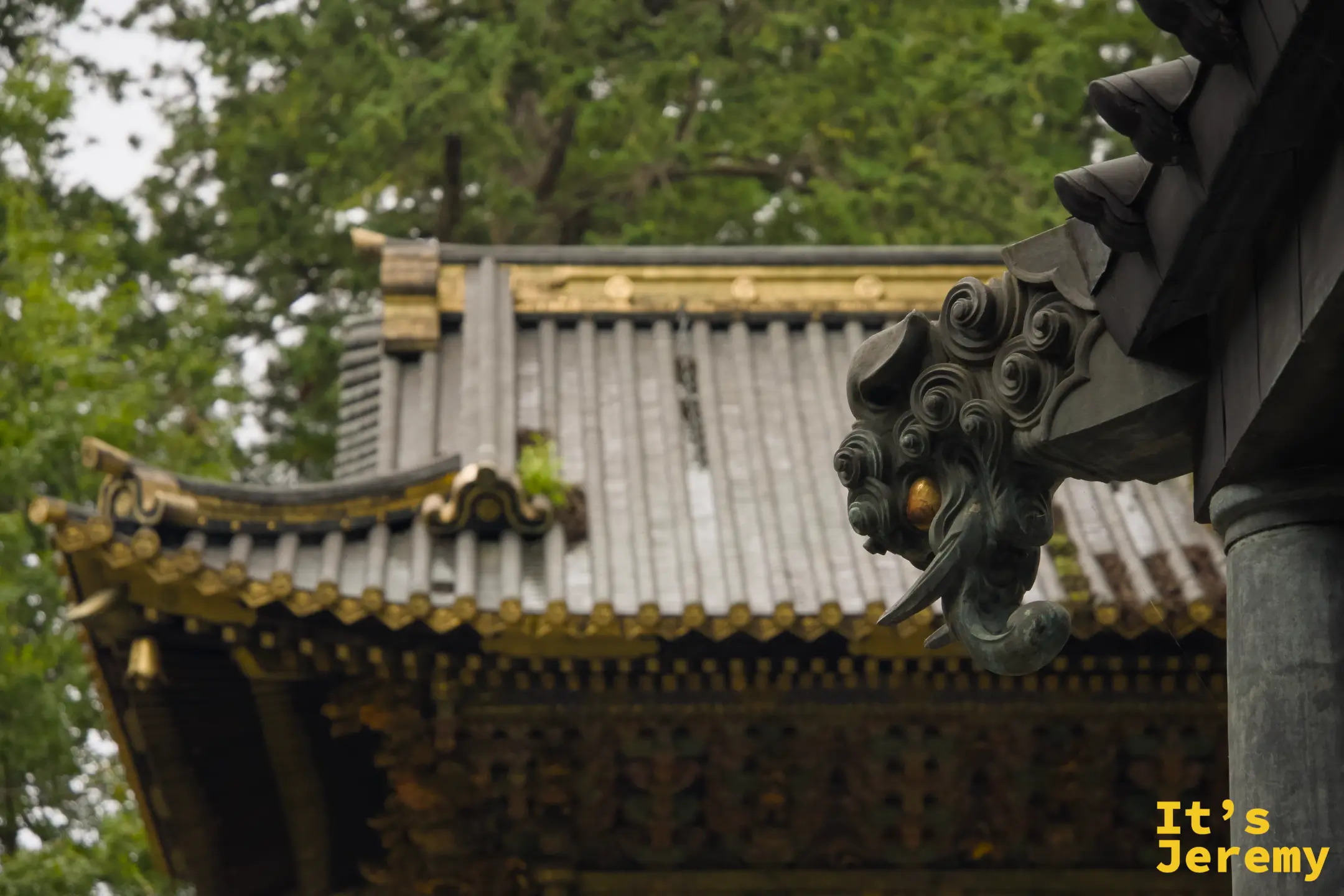 境內某棟建築上的銅製龍頭獸面飾件，氧化後呈墨綠色，背景是另一棟建築的屋頂