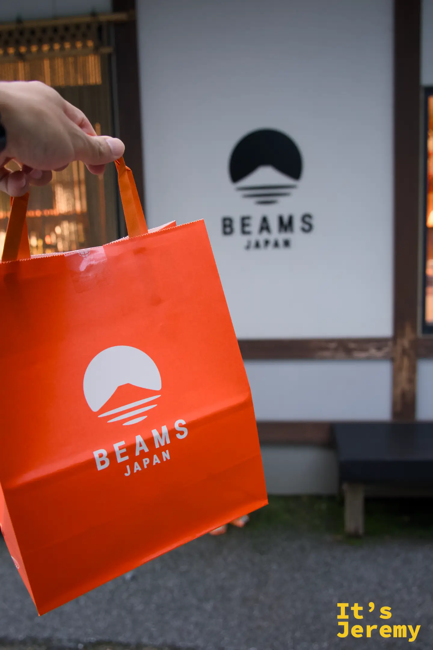手持 BEAMS JAPAN 橘色購物袋特寫，背景是 BEAMS JAPAN 招牌