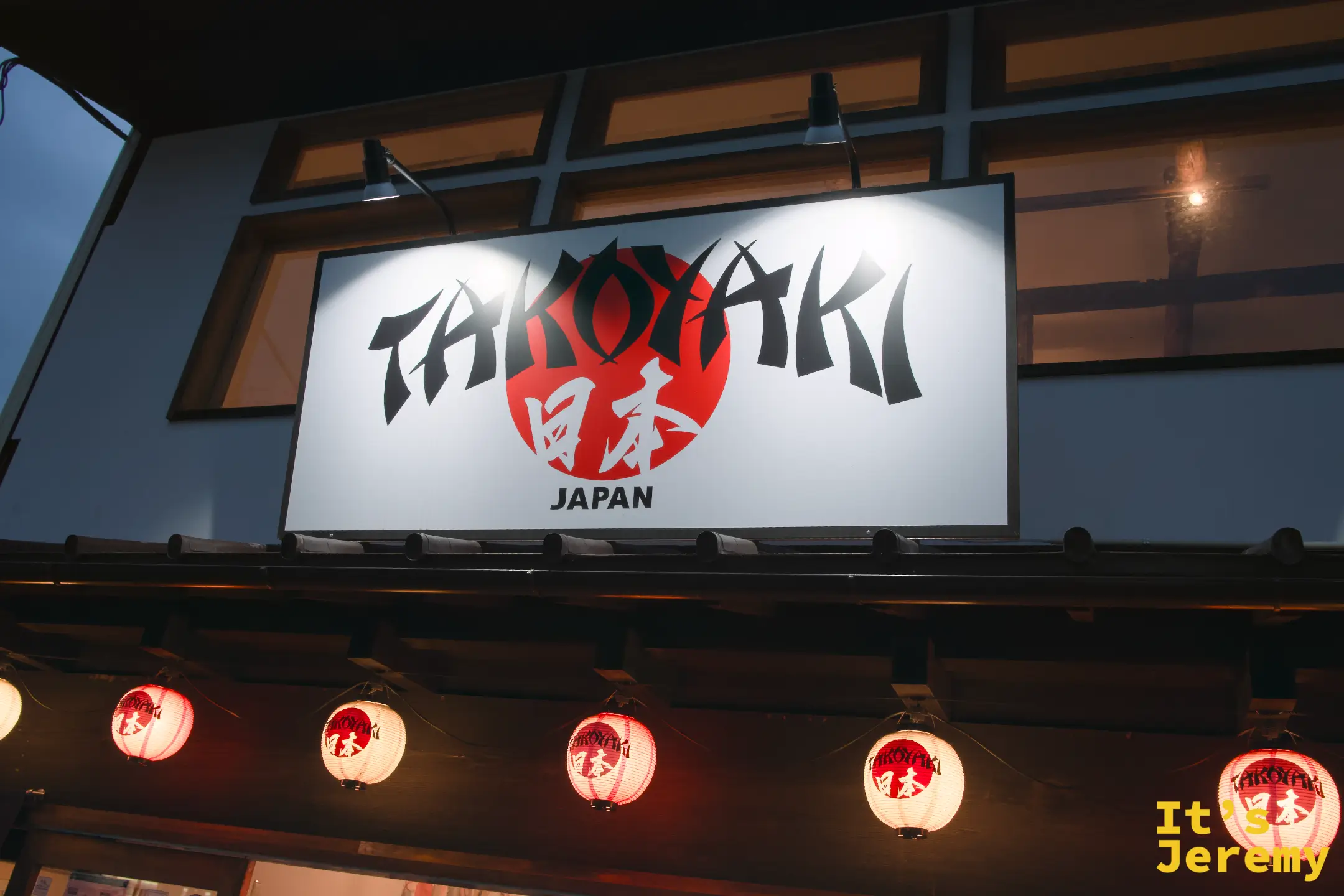 Takoyaki Japan 招牌夜晚打燈，黑白大字「TAKOYAKI JAPAN」配紅日圓設計