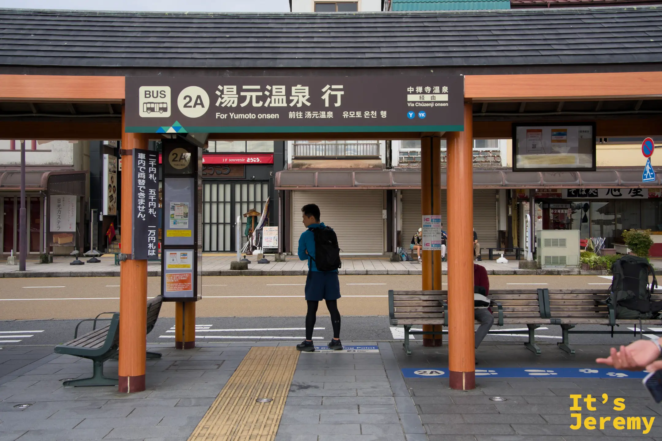 候車亭，背著背包的路人站在「BUS 2A 湯元温泉 行」標示下等車