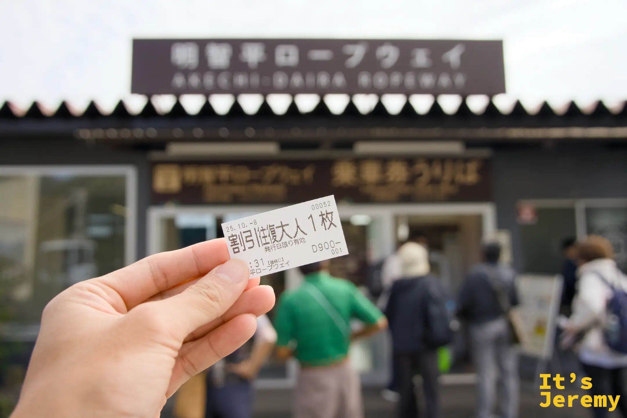 手持當天購買的往復乘車券，背景是售票處入口與排隊的旅人