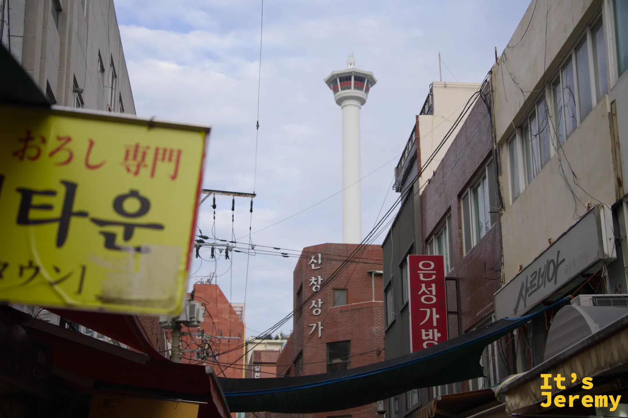 釜山塔在市場街頭的黃色招牌與店家招牌之間悄悄探出頭