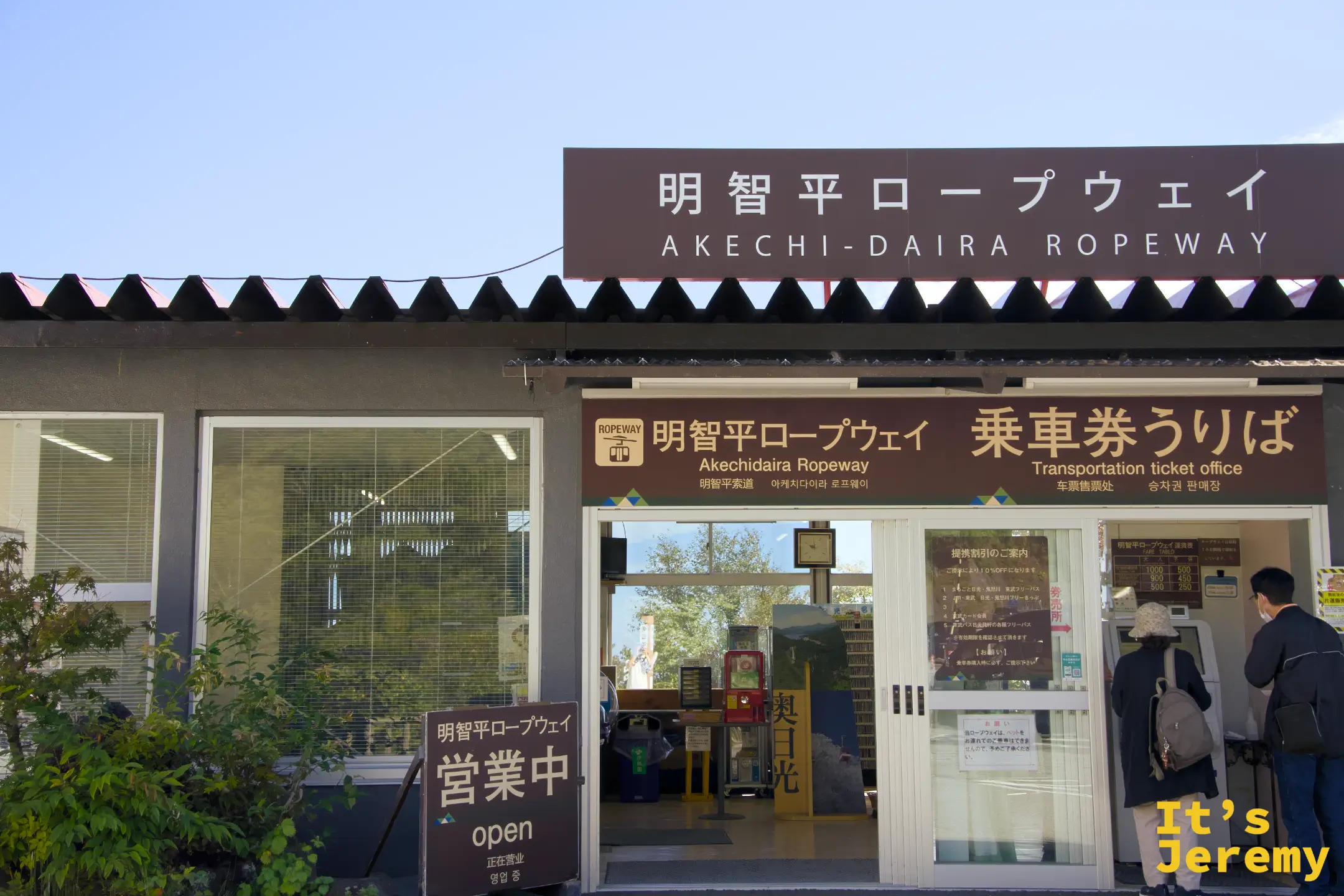 明智平ロープウェイ售票口外觀，深咖啡色招牌，晴天藍空下「営業中」旗幟飄揚