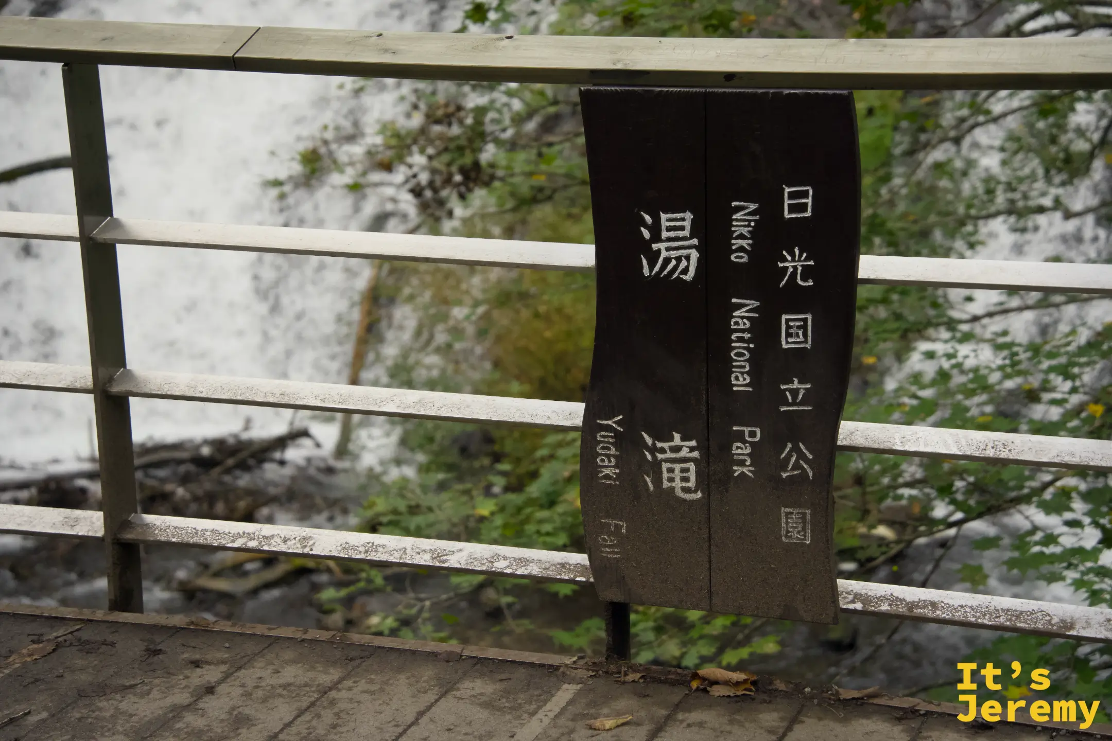 欄杆上的「日光国立公園 湯滝 Yudaki Fall」黑色標牌，背後是流動的水幕