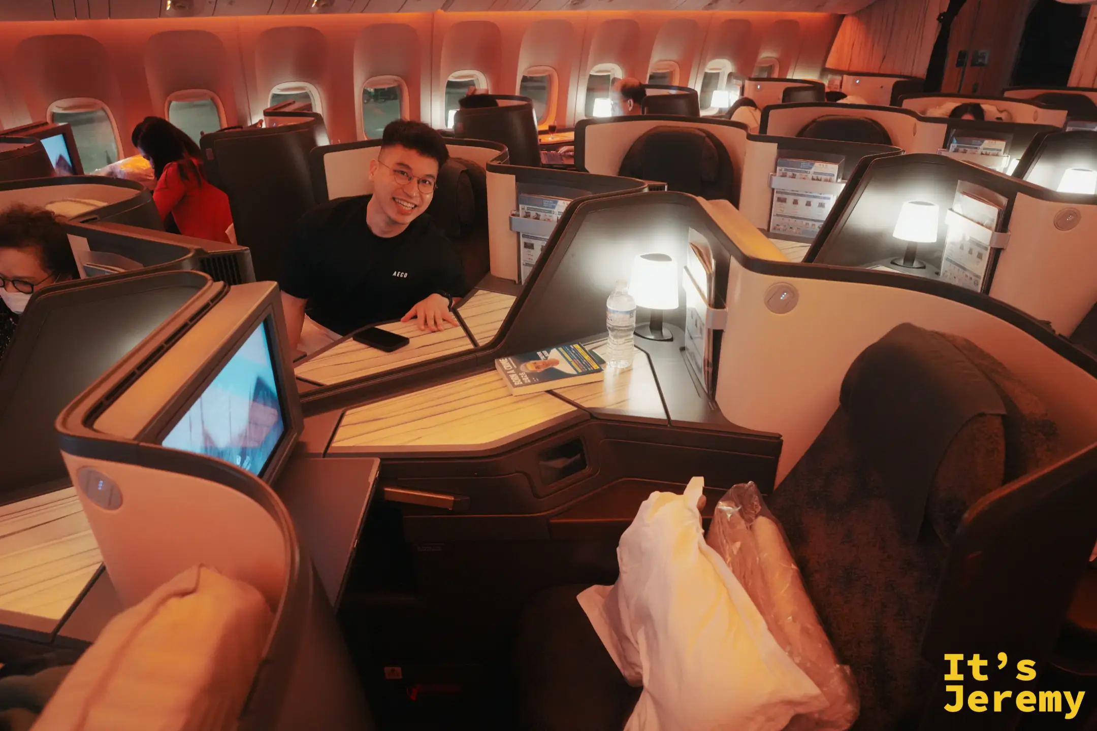 Jeremy 坐在中華航空商務艙座位，桌板上放著手機與礦泉水，笑得有點靦腆