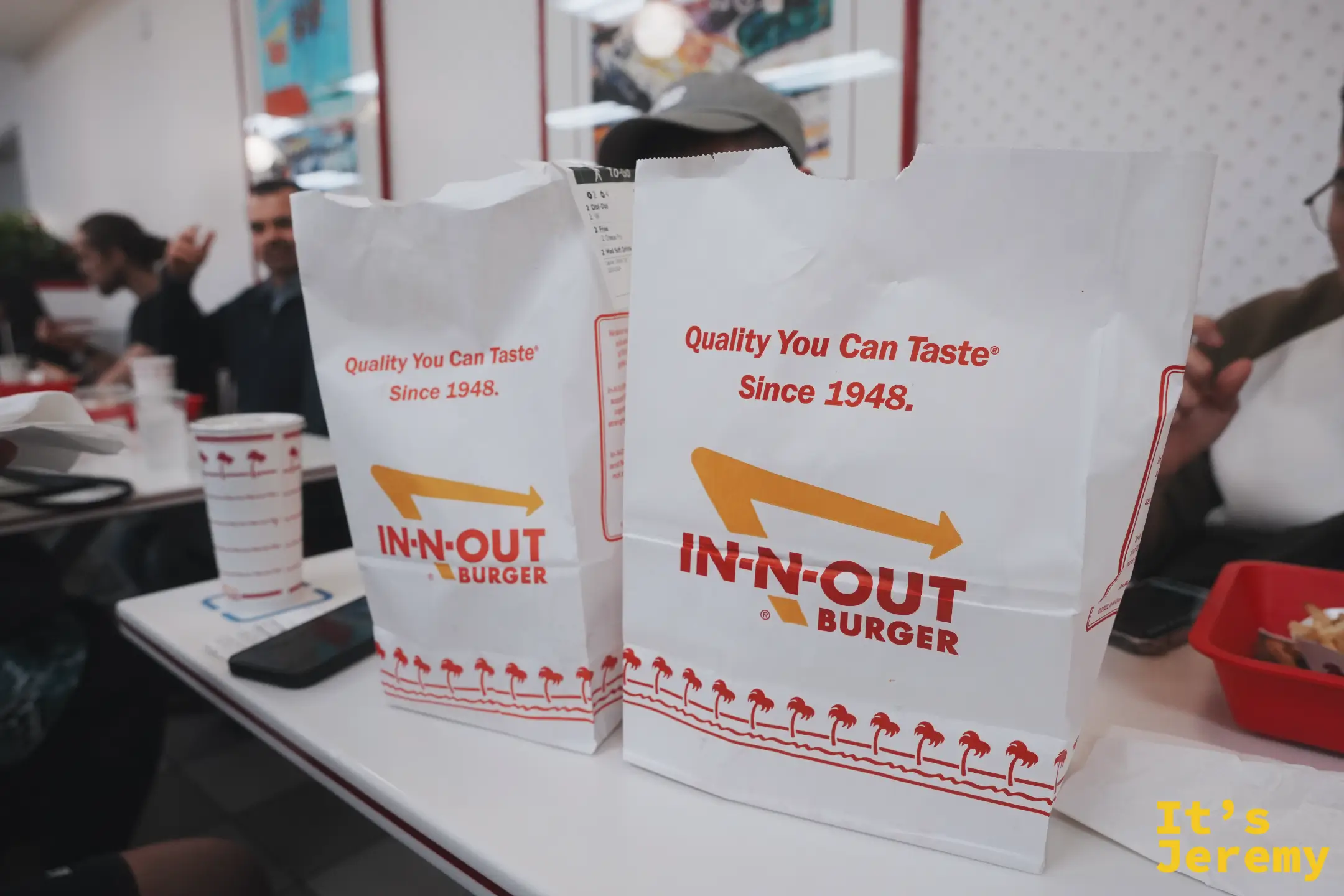 桌上兩個印著 Quality You Can Taste Since 1948 的白色 In-N-Out 外帶紙袋