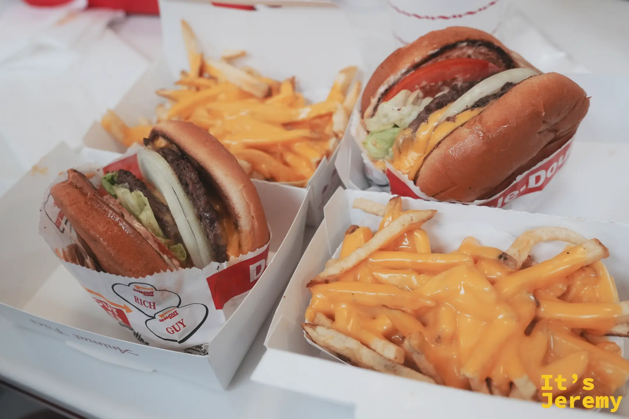 兩份 In-N-Out Double-Double 漢堡與兩盒鋪滿起司的薯條，配紅白棕櫚樹圖案的紙杯