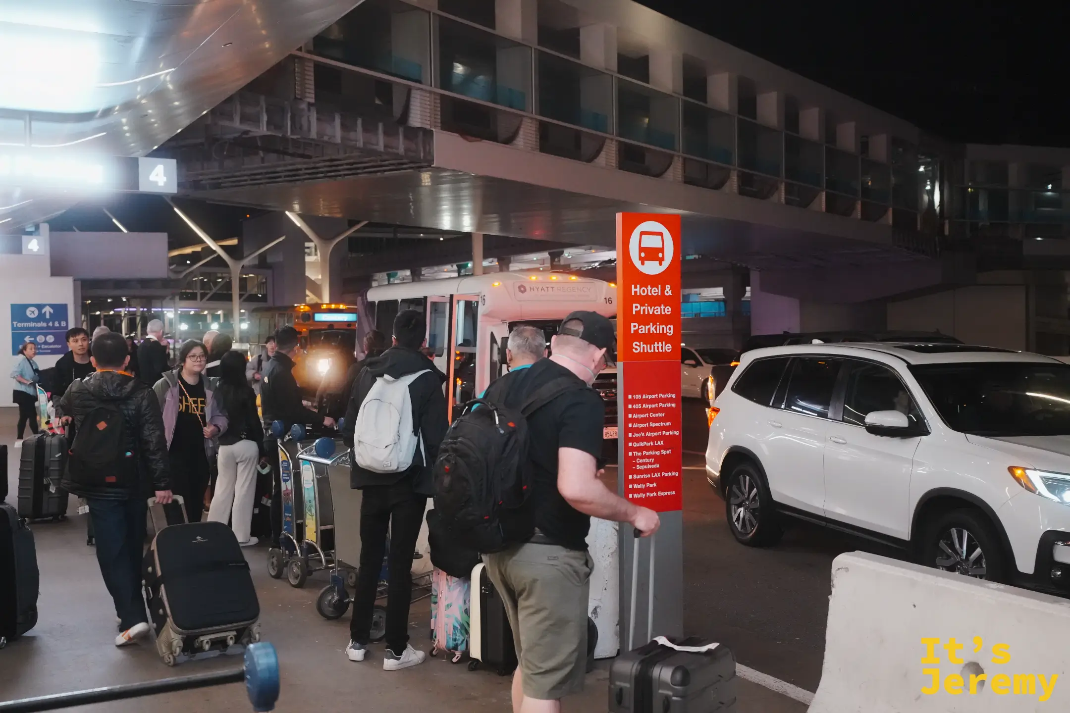 紅色「Hotel & Private Parking Shuttle」站牌下，一群拖著行李的旅客等著各家飯店接駁車