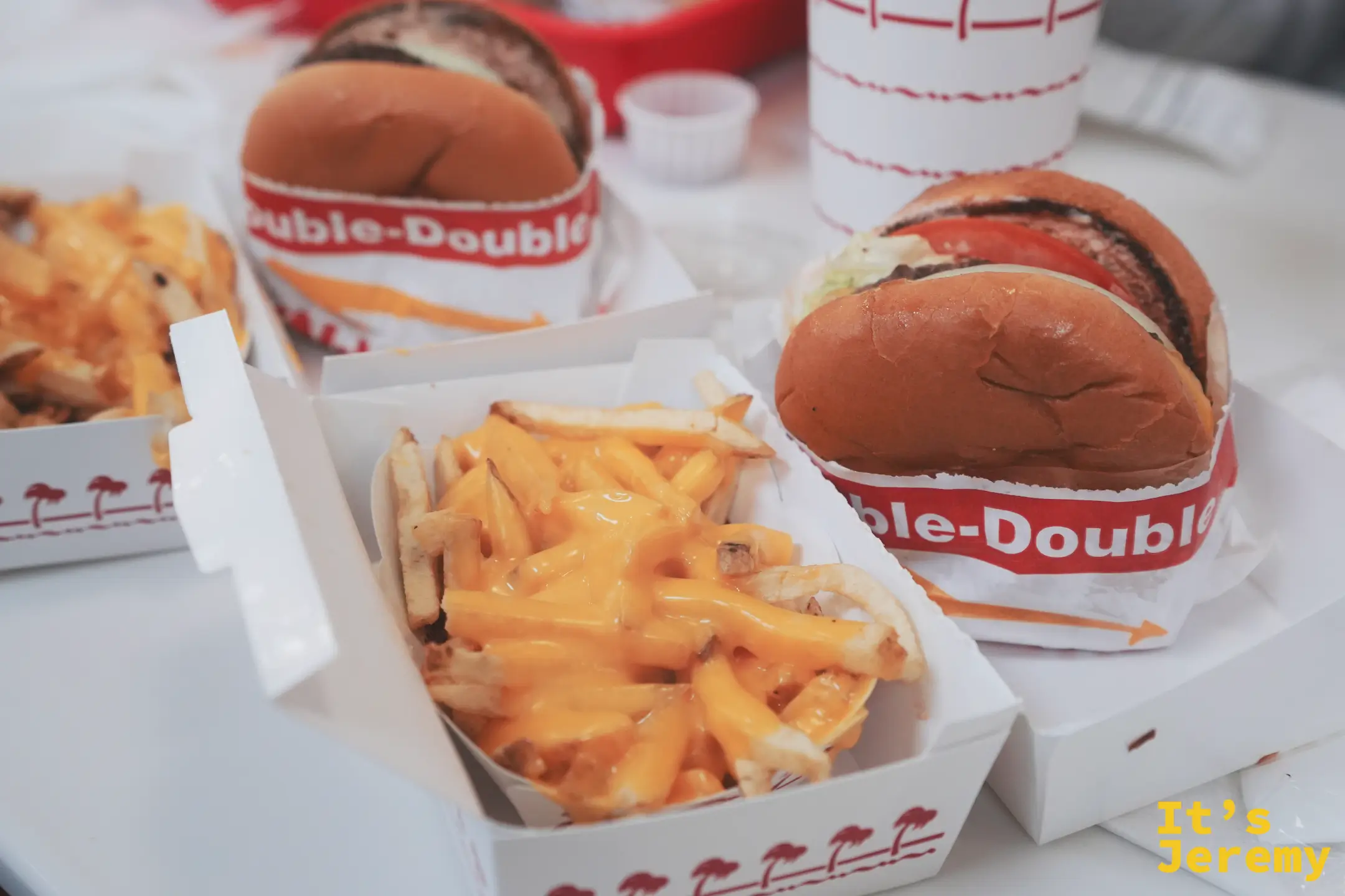 兩份 Double-Double 與兩盒起司薯條的近距離俯拍，起司醬淋滿薯條