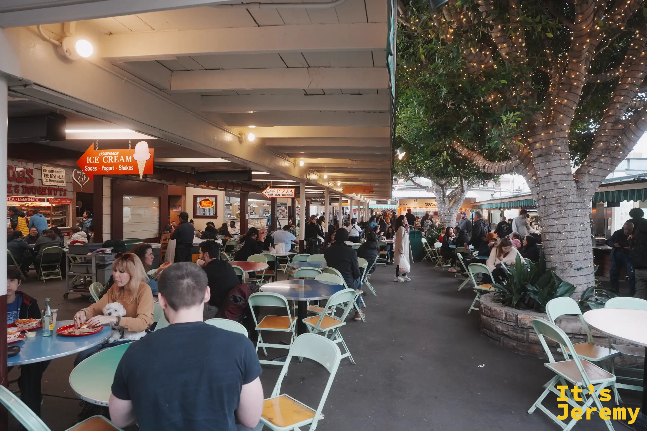 Farmers Market 串著小燈的用餐區，人們在彩色摺疊椅上吃東西