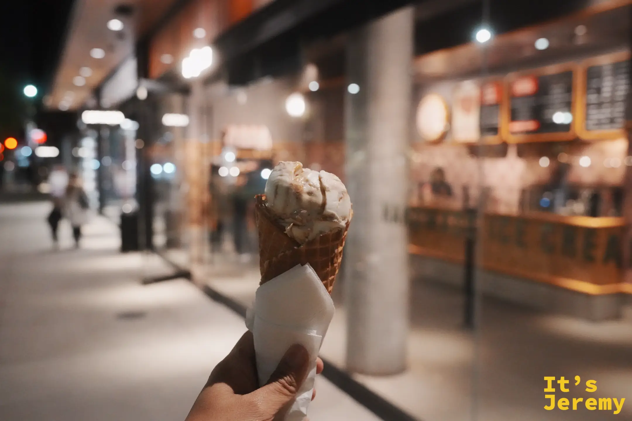 街邊手拿 Salt & Straw 脆皮蛋捲冰淇淋，背景是店面暖燈