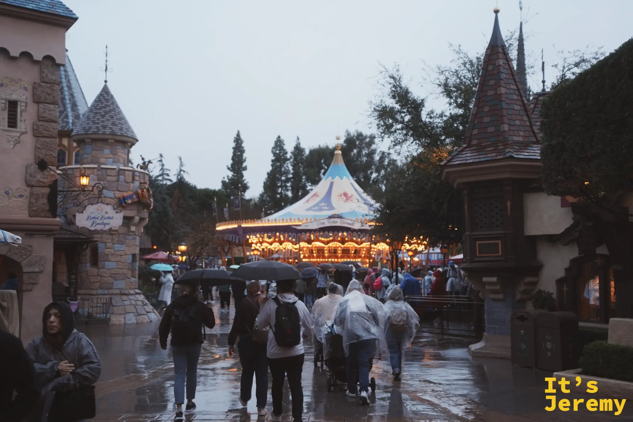 傍晚雨中的夢幻世界，亮著暖黃燈的旋轉木馬與城堡塔樓