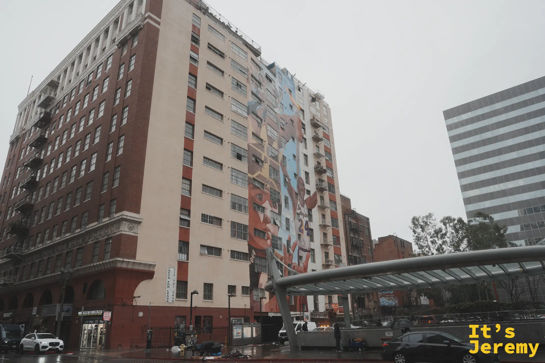 DTLA 街角一整棟大樓側牆上的科比 24 號球衣巨幅壁畫，雨天濕亮的路面