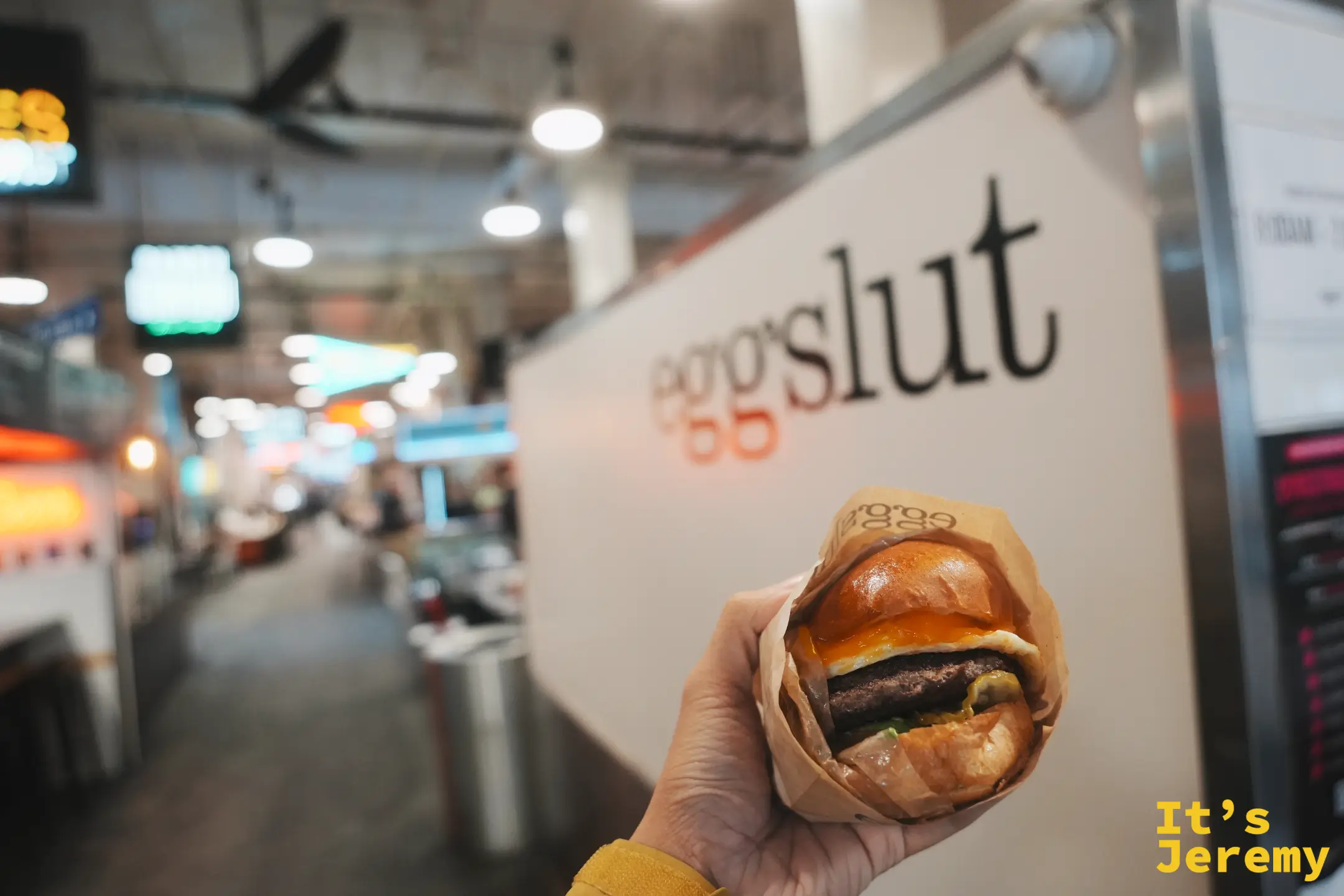 手拿 Eggslut 溏心蛋堡站在 eggslut 招牌前