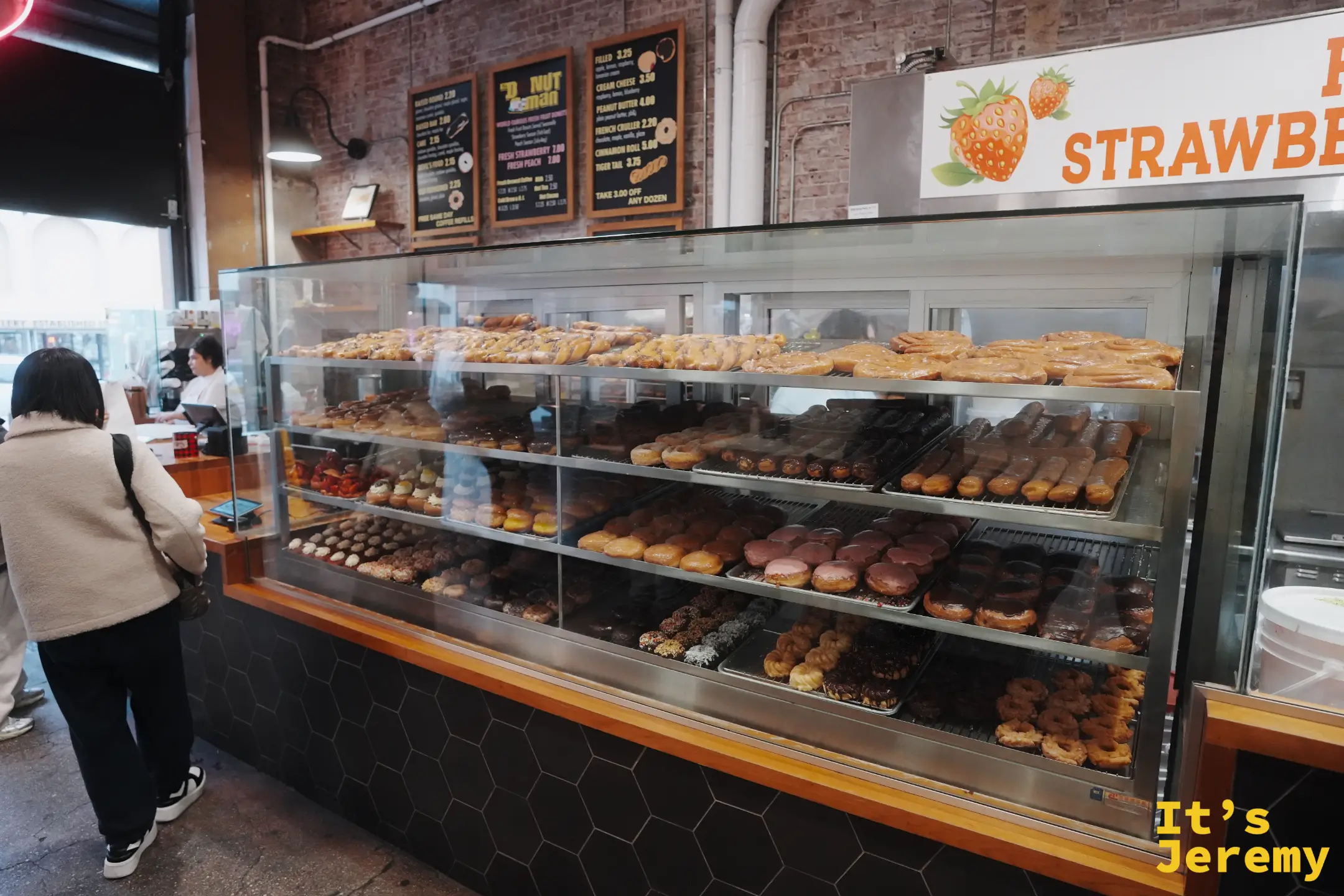 The Donut Man 甜甜圈櫃，整排糖霜與巧克力甜甜圈，牆上有草莓招牌