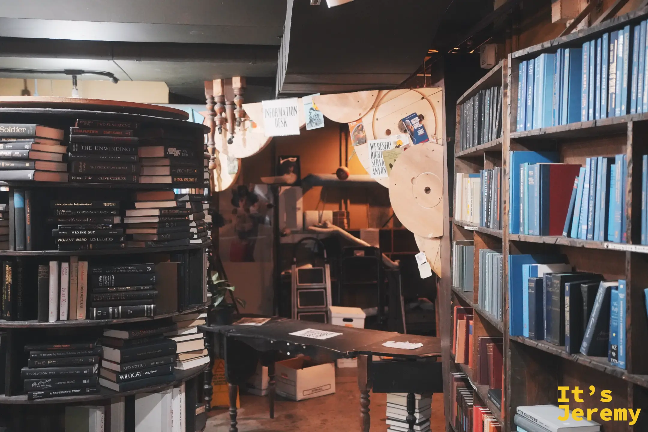 The Last Bookstore 圓形旋轉書架堆成塔狀，牆面是藍色書封舊書與 INFORMATION DESK 牌子