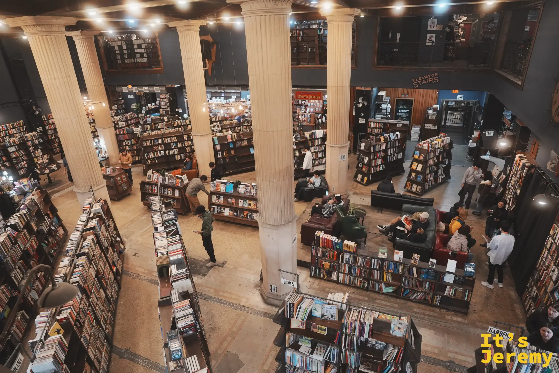 從二樓俯瞰 The Last Bookstore 大廳，古典圓柱、綿延書架與地面上的讀者