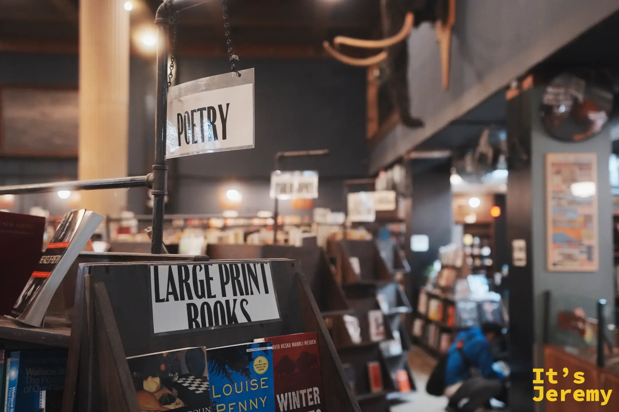 The Last Bookstore 懸掛的 POETRY 分區吊牌與 LARGE PRINT BOOKS 立牌，上方有長毛象標本
