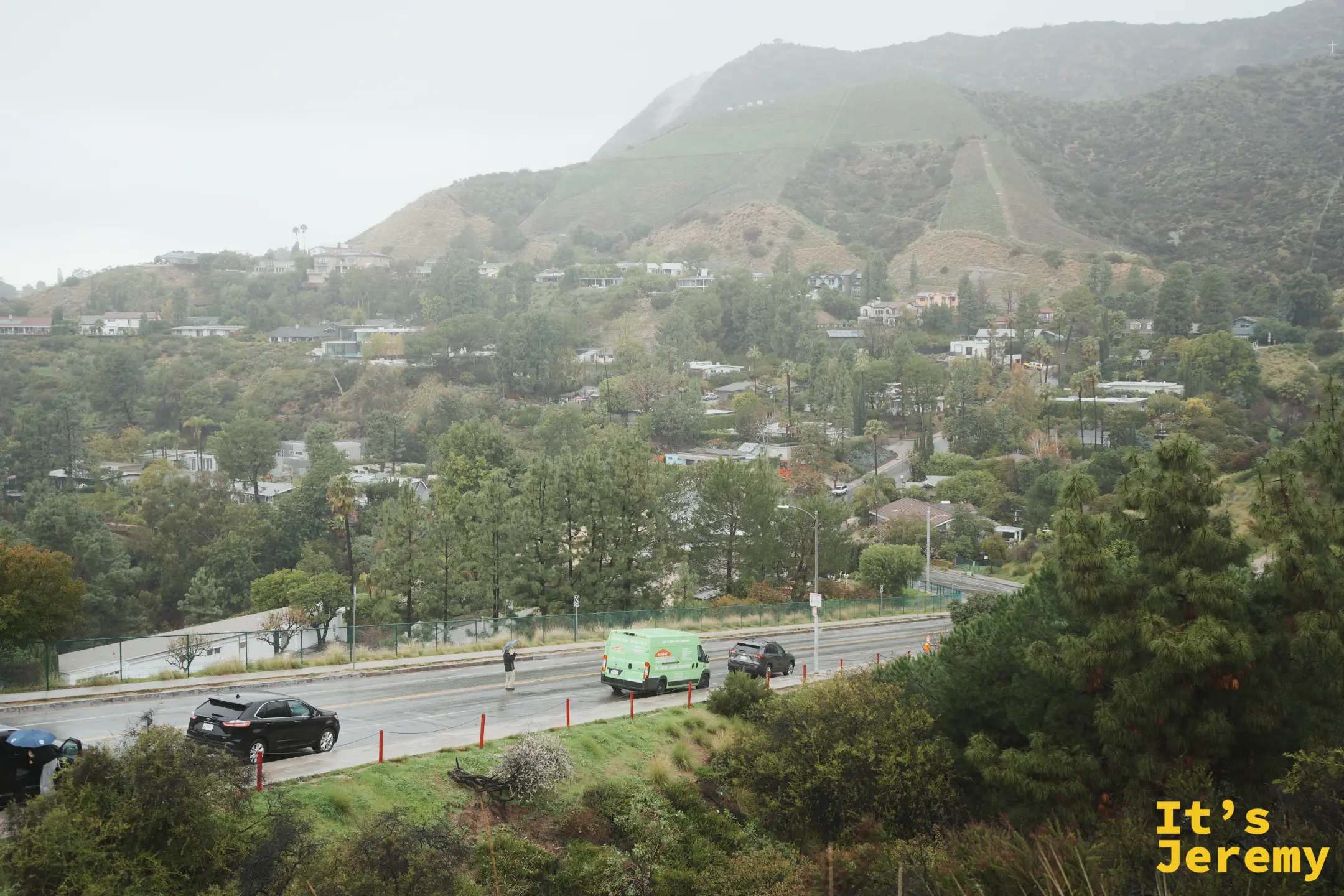 好萊塢山住宅區與山谷，路上有車輛行經，遠處山頂雲霧繚繞