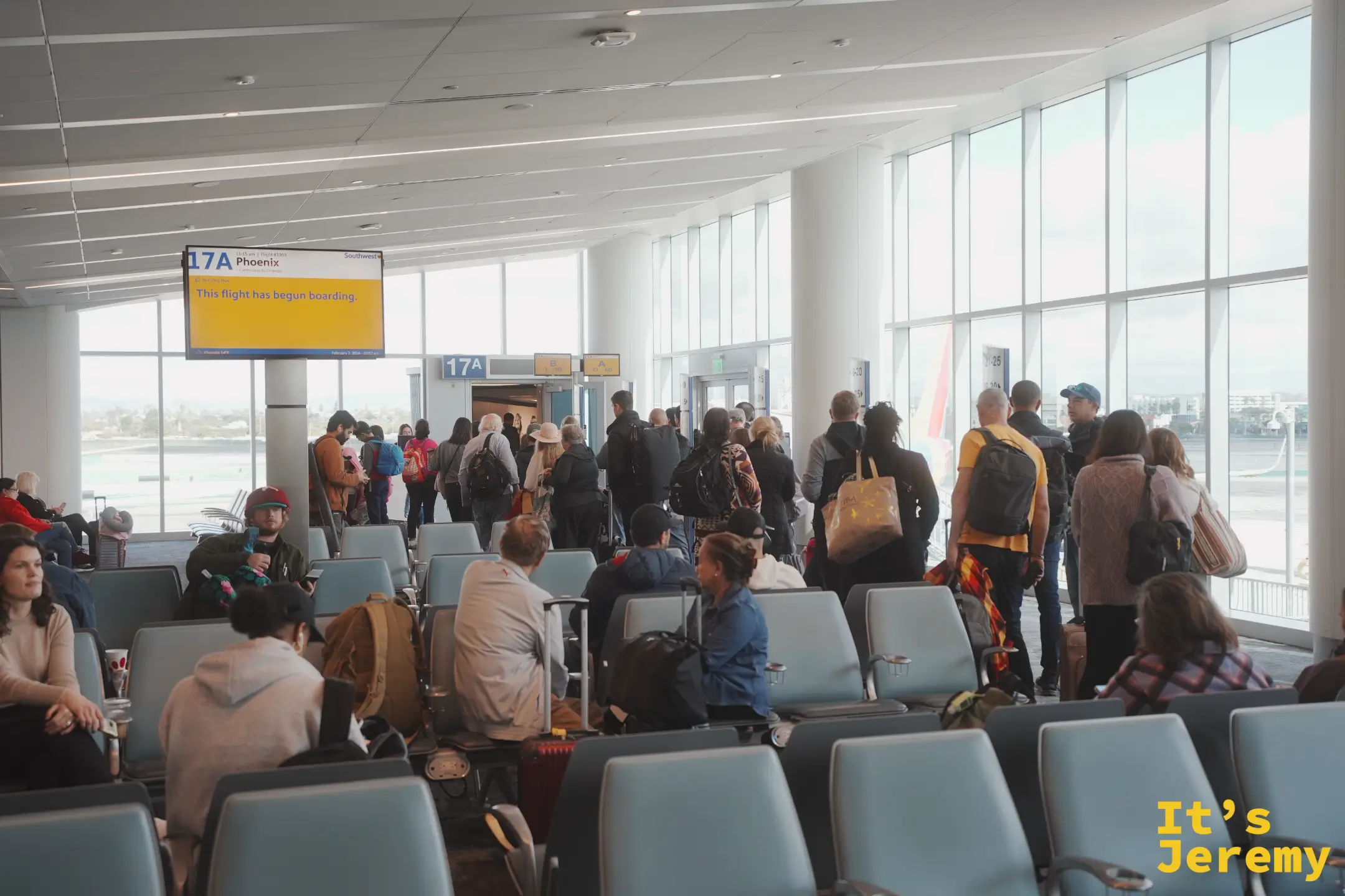 LAX 17A 登機門的黃色螢幕顯示「17A Phoenix — This flight has begun boarding」，一群南西航空旅客正排隊等候登機，其他人坐在候機椅上