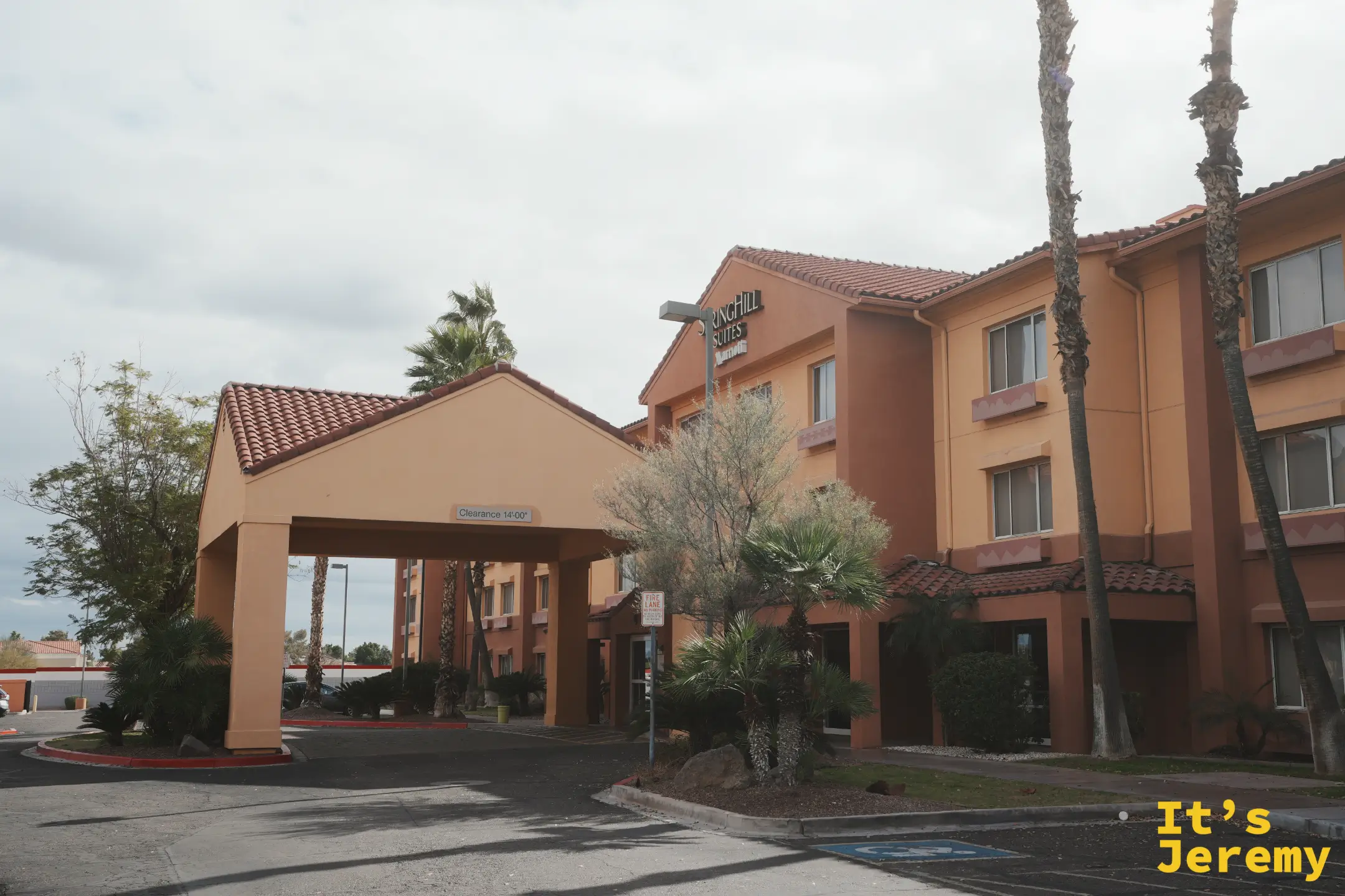 沙漠風格的 SpringHill Suites 旅館外觀，米色與磚紅建築、紅瓦屋頂與迎賓車道門廊，四周種著棕櫚樹