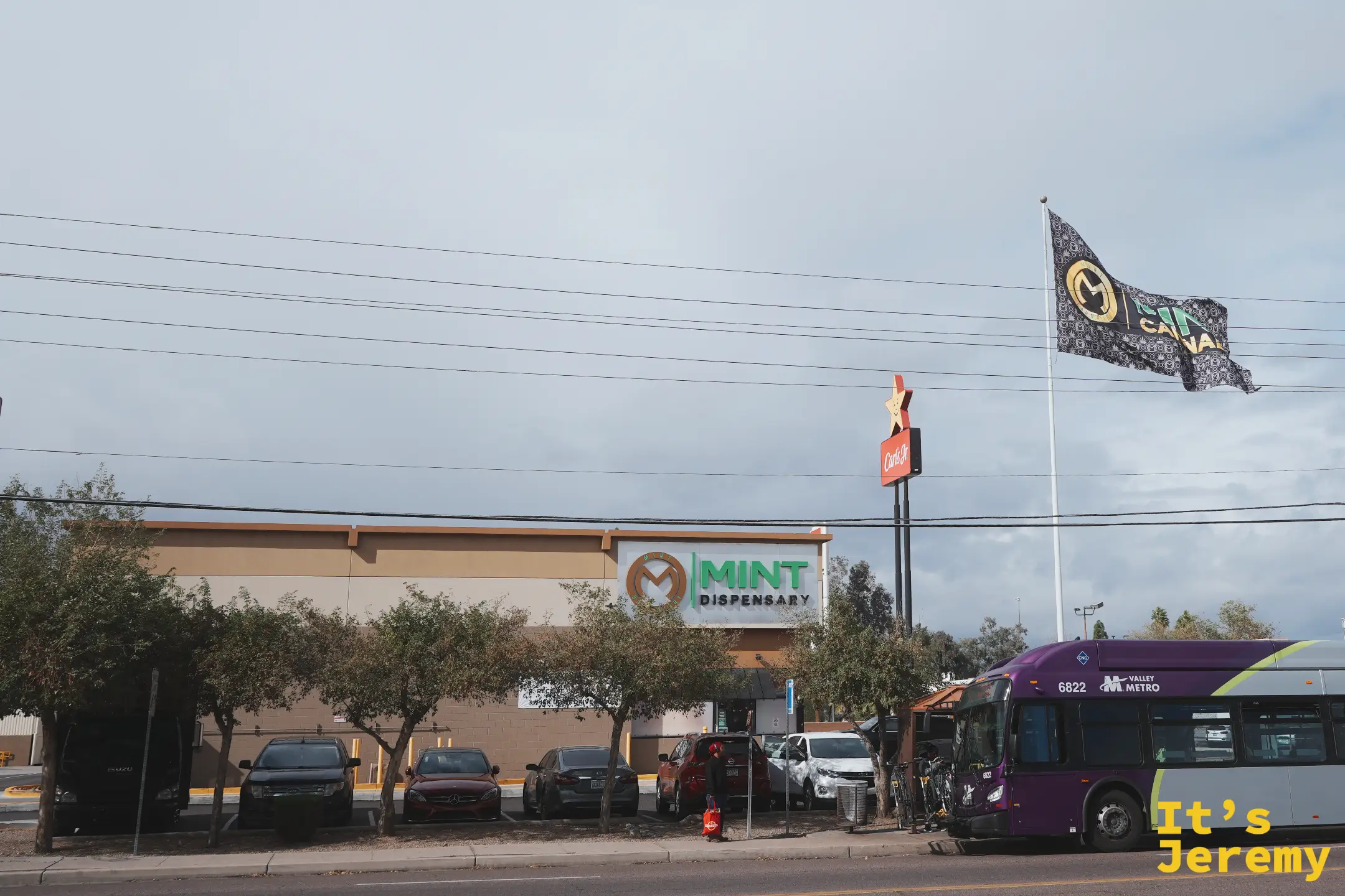 Mint Cannabis 坦佩店的街景遠照，米色建築、品牌大旗與一旁的 Valley Metro 紫色公車