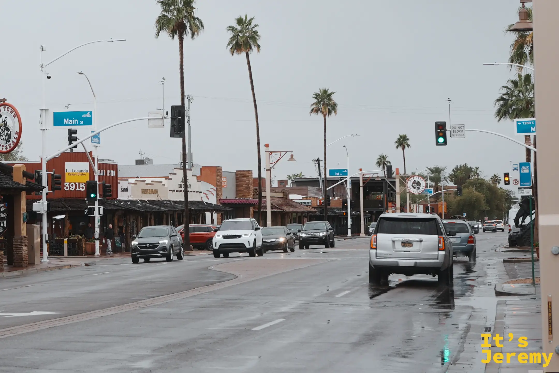 雨中的斯科茨代爾老城 Main St 與 Scottsdale Rd 路口，濕亮的路面、棕櫚樹與 Old Town Scottsdale 圓形招牌