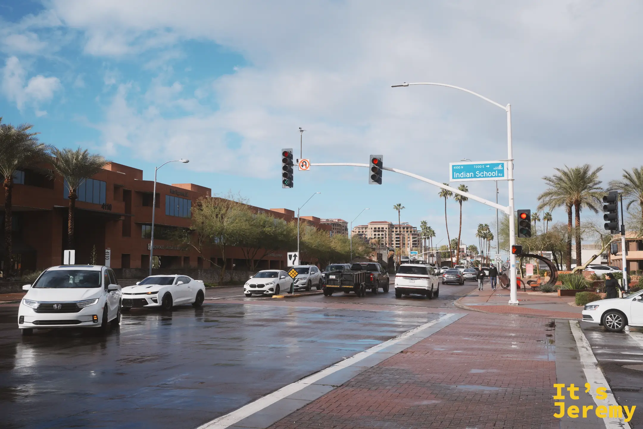 雨中的 Indian School Rd 路口街景，路牌、辦公大樓與濕亮的紅磚人行道