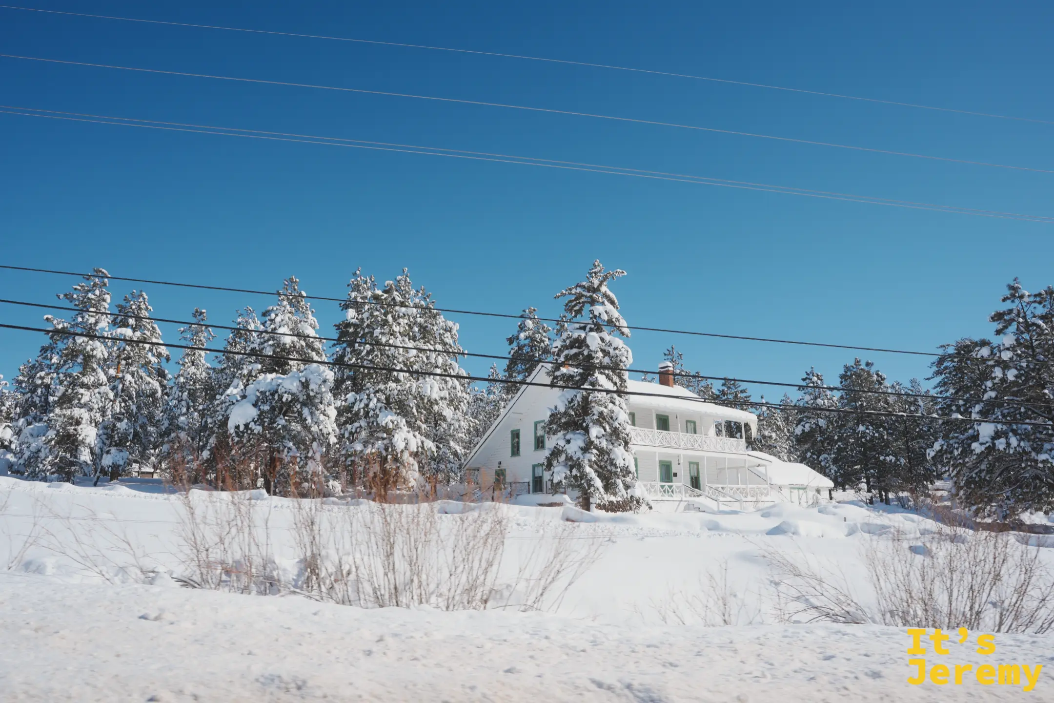 往北公路旁一棟白色兩層木屋，藏在掛滿雪的松林後面，前方是深厚的積雪