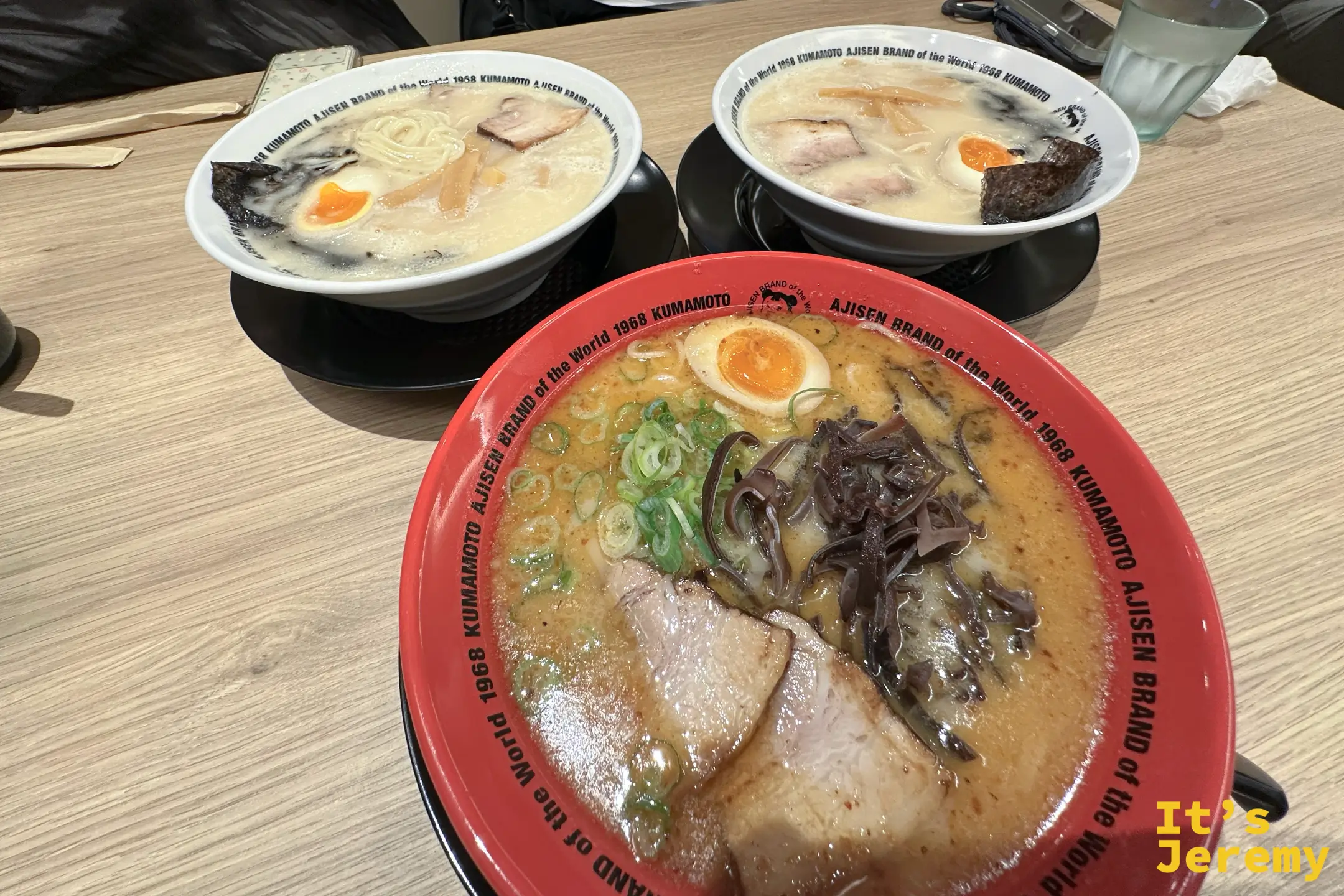 店內木桌上三碗拉麵並排，前方是紅碗黑拉麵，後方兩碗白碗味千豚骨