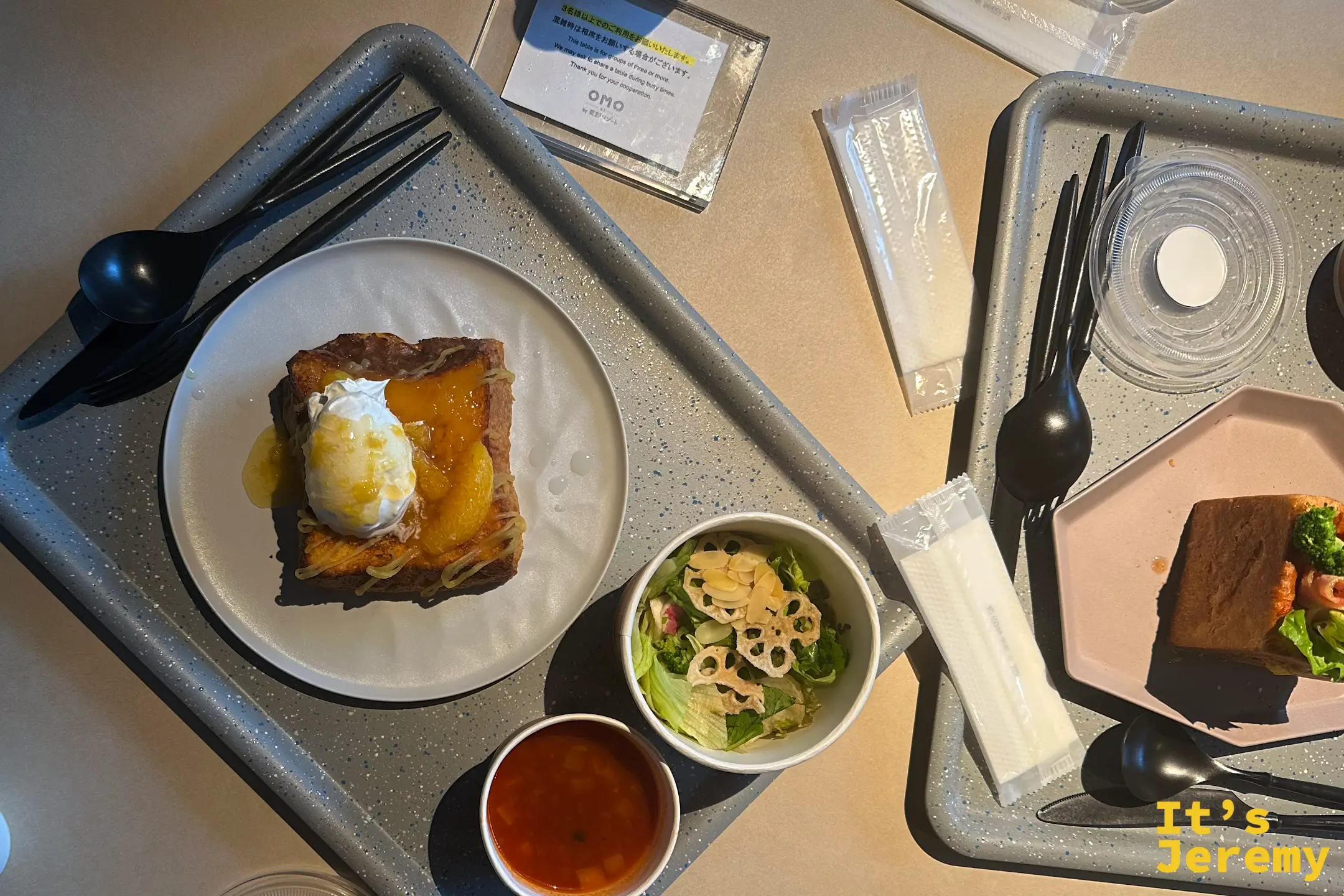 OMO5 熊本套餐式早餐俯拍，灰色托盤上有一盤柳橙醬法式吐司、一杯生菜沙拉與一杯番茄湯，旁邊放著 OMO by 星野 的桌卡