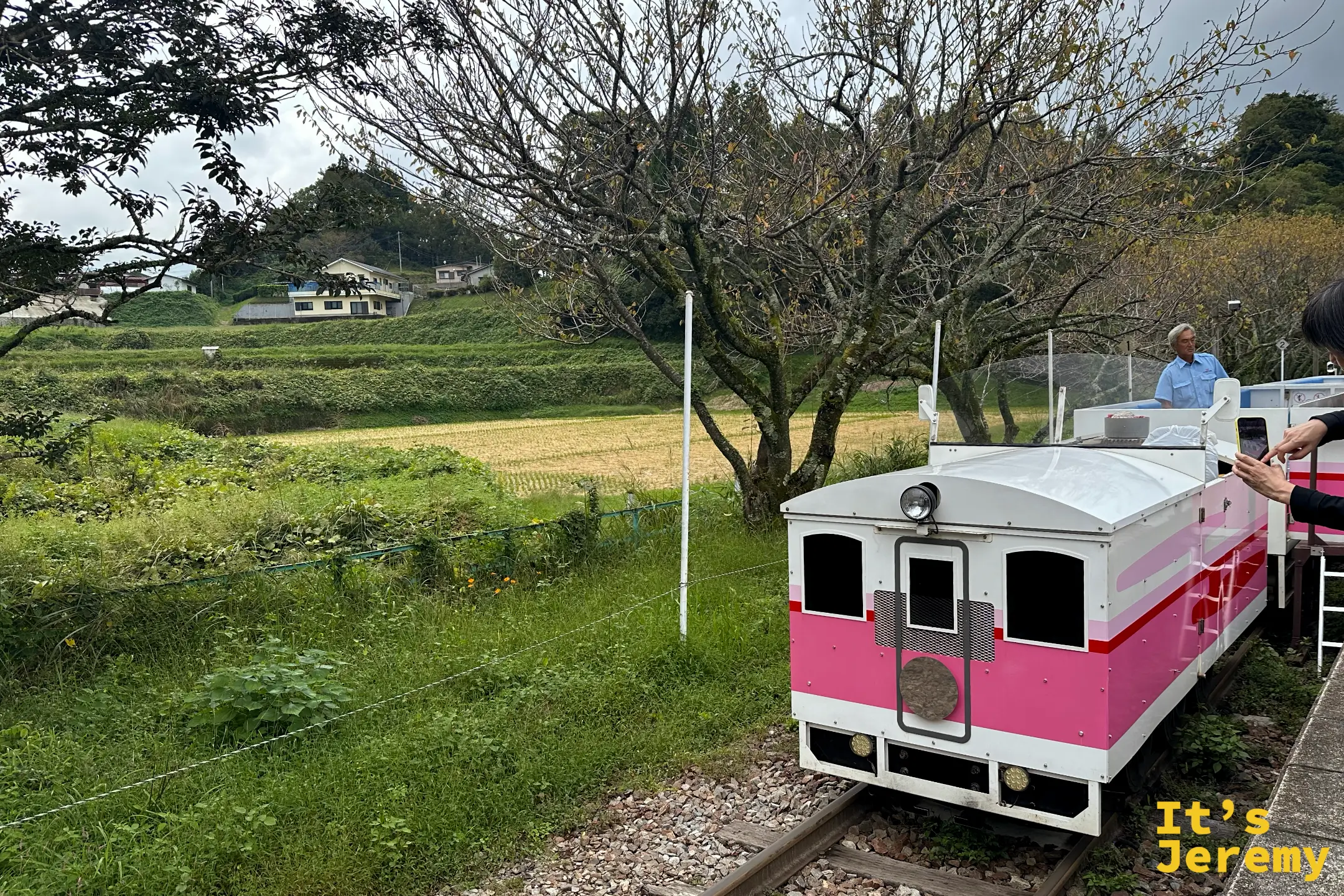 Grand Super Cart 行駛在軌道上，司機穿藍色制服，背景是稻田與民宅