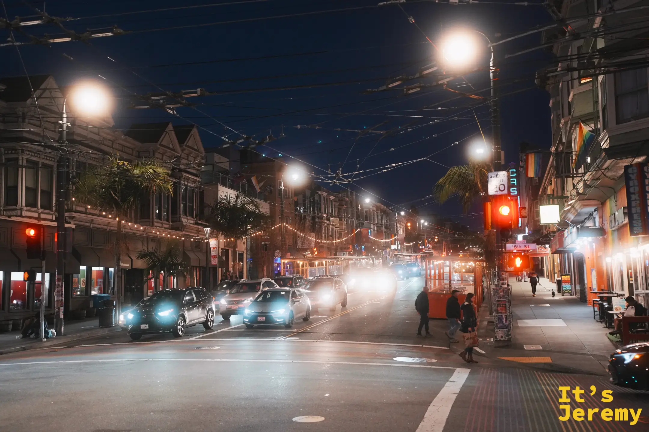 卡斯楚街與 18th St 交會的夜景，車燈與街燈連成一片，人行道上人來人往，店家霓虹亮起
