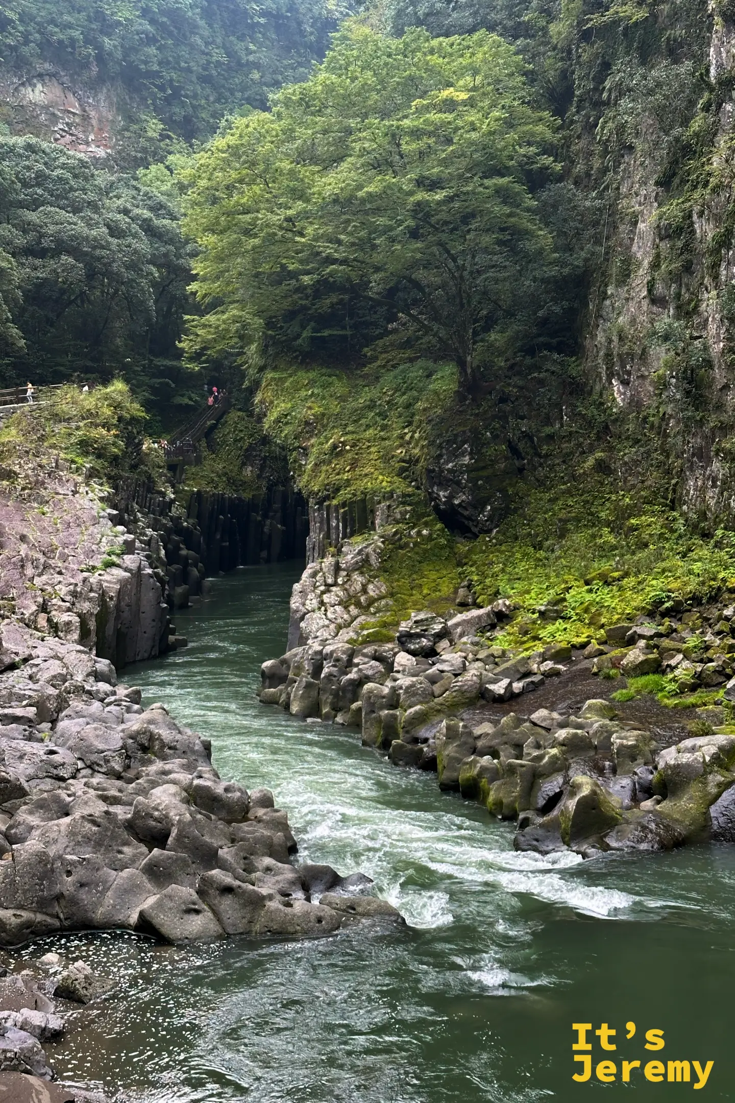 高千穂峡的柱狀節理石壁與湍急溪流，上方步道有遊客