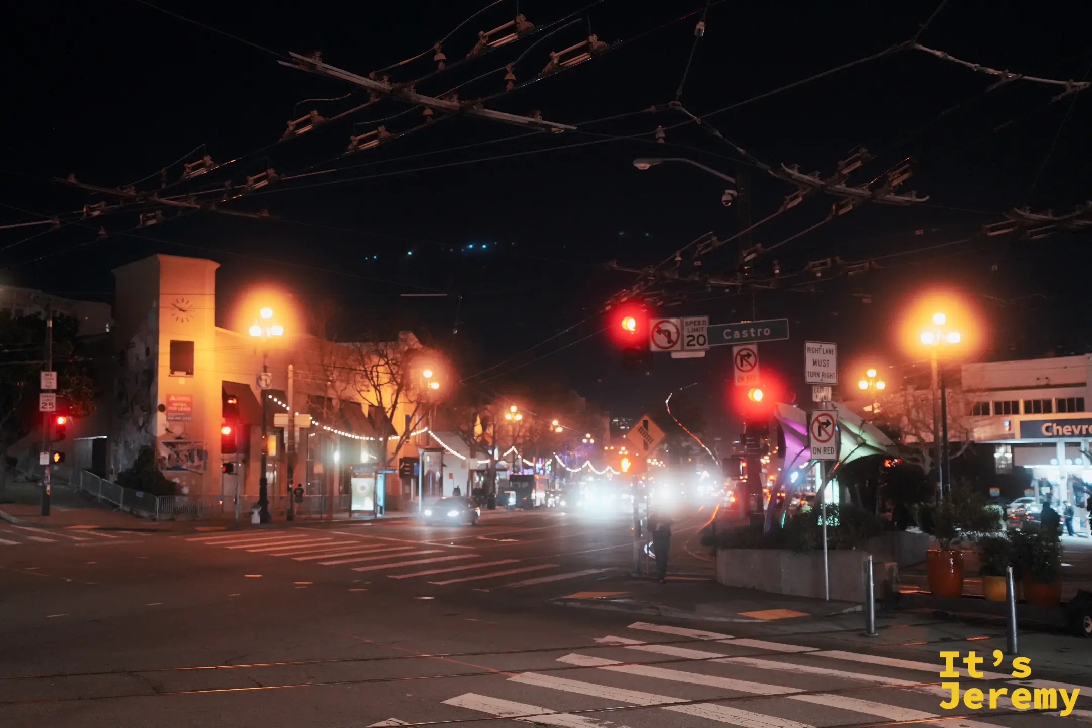 卡斯楚區 Castro 與 Market 街口的夜景，黃色鐘樓建築立在路口，遠處是點著燈的街道與 Sutro 電視塔