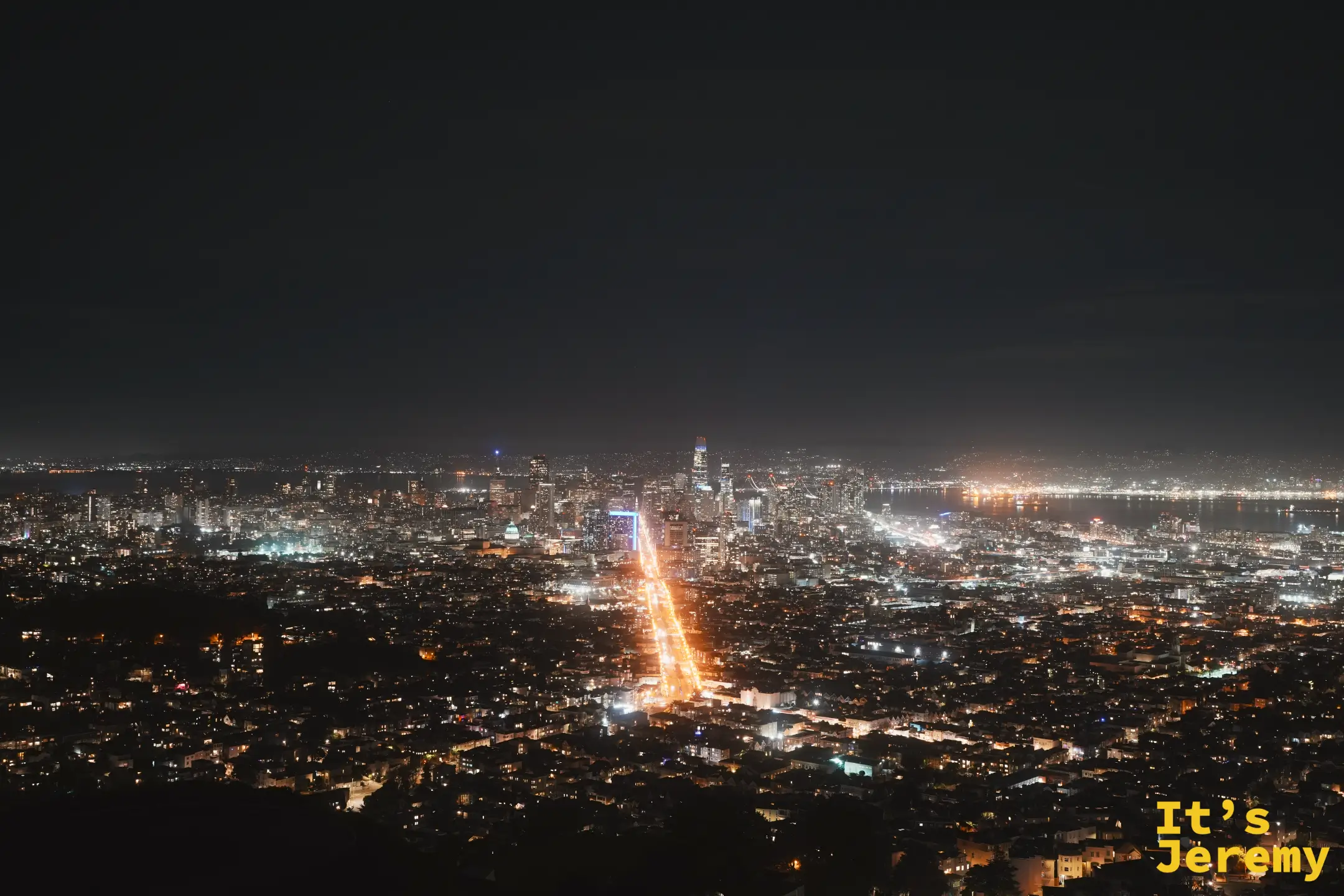舊金山市中心夜景，Salesforce Tower 等高樓在天際線上發亮，Market Street 的金線筆直射向樓群，遠處是海灣燈火