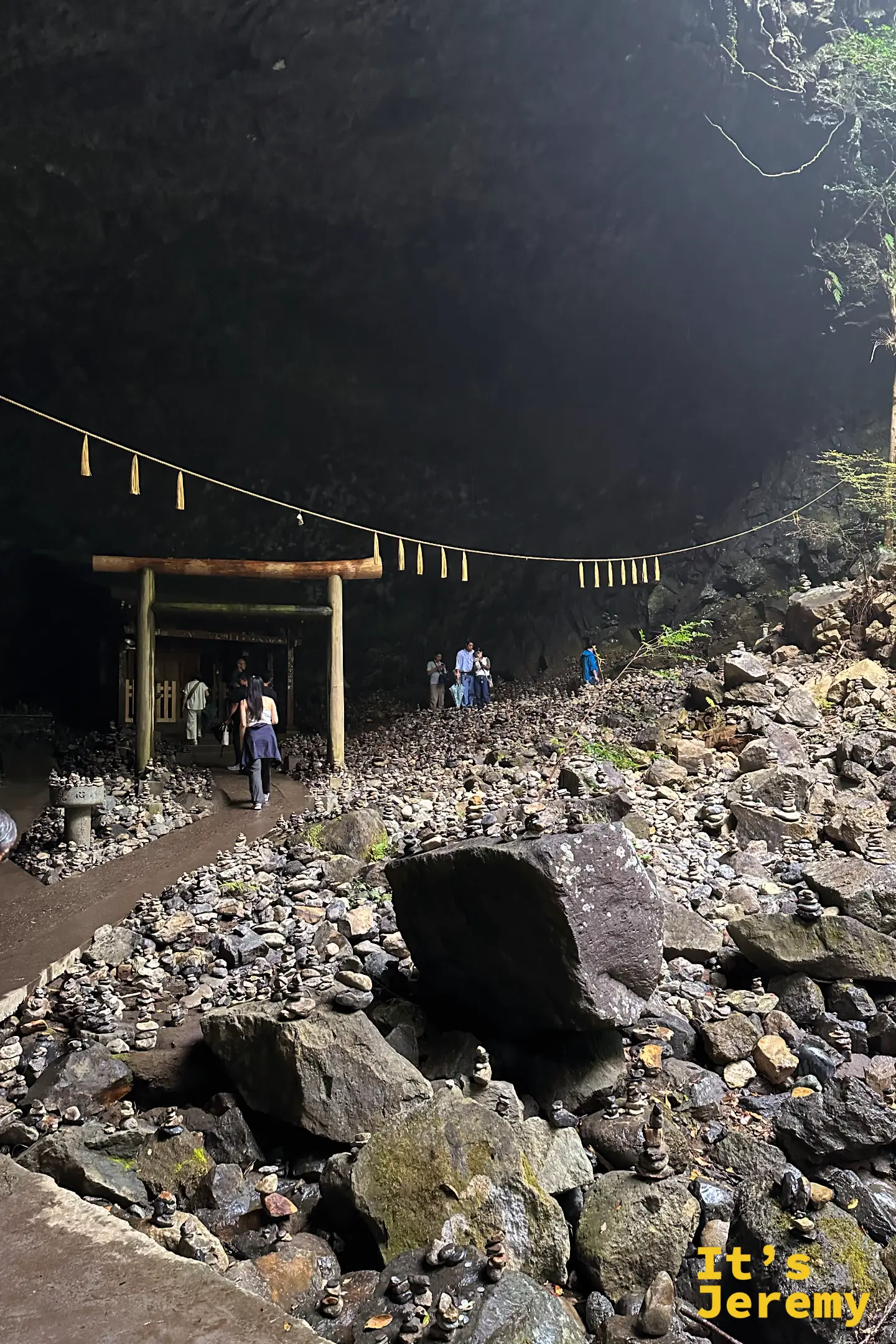 天安河原的仰慕窟，木造鳥居與小祠立在洞內，遊客散布在石堆之間